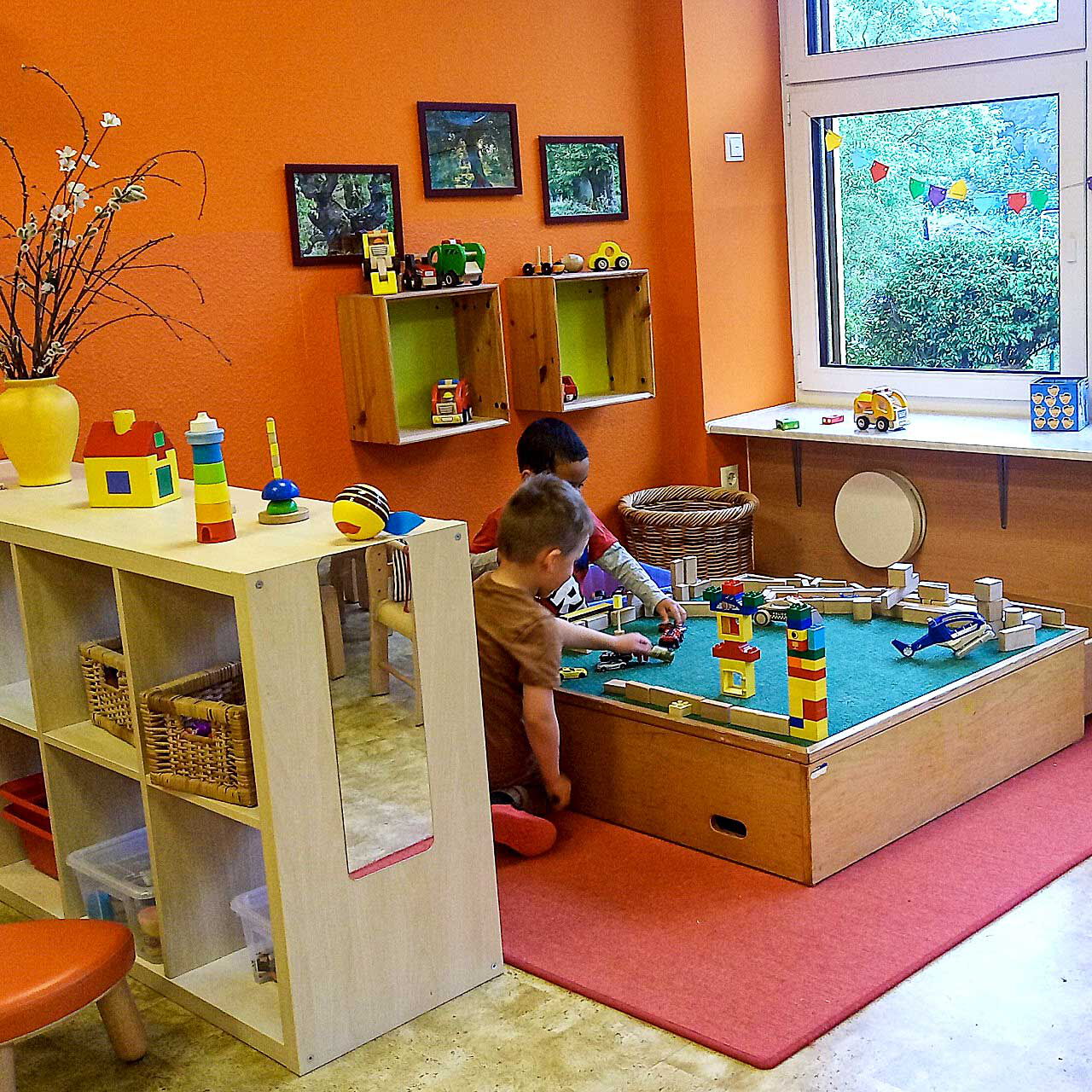In der Ecke des Raumes ist ein Bauspiel auf dem zwei Kleinkinder mit Bausteinen spielen und bauen.