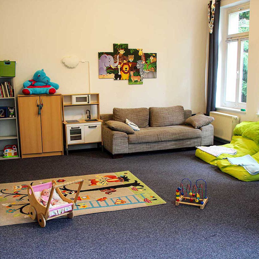 Der Spielbereich mit einem Sofa, einer Kinderspielküche und viel Spielzeug in einem Regal und auf dem Fußboden.