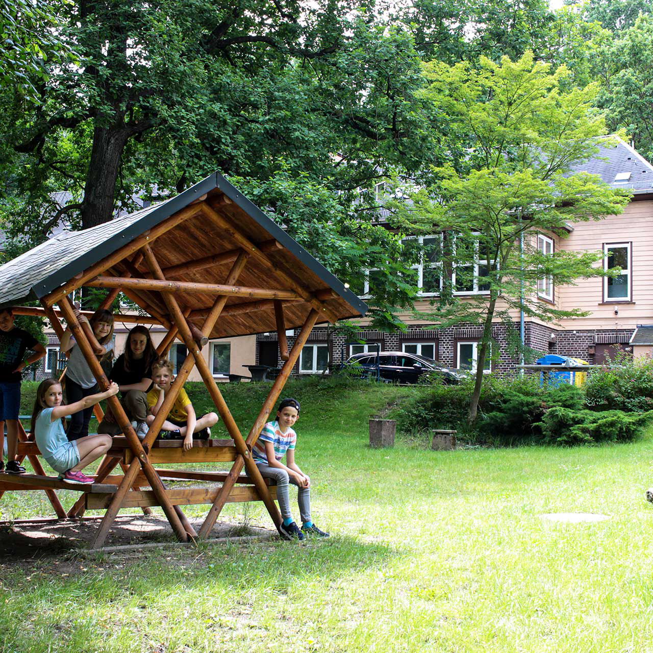 Im Vordergrund stehend eine überdachte Sitzgruppe und im Hintergrund das Haupthaus.