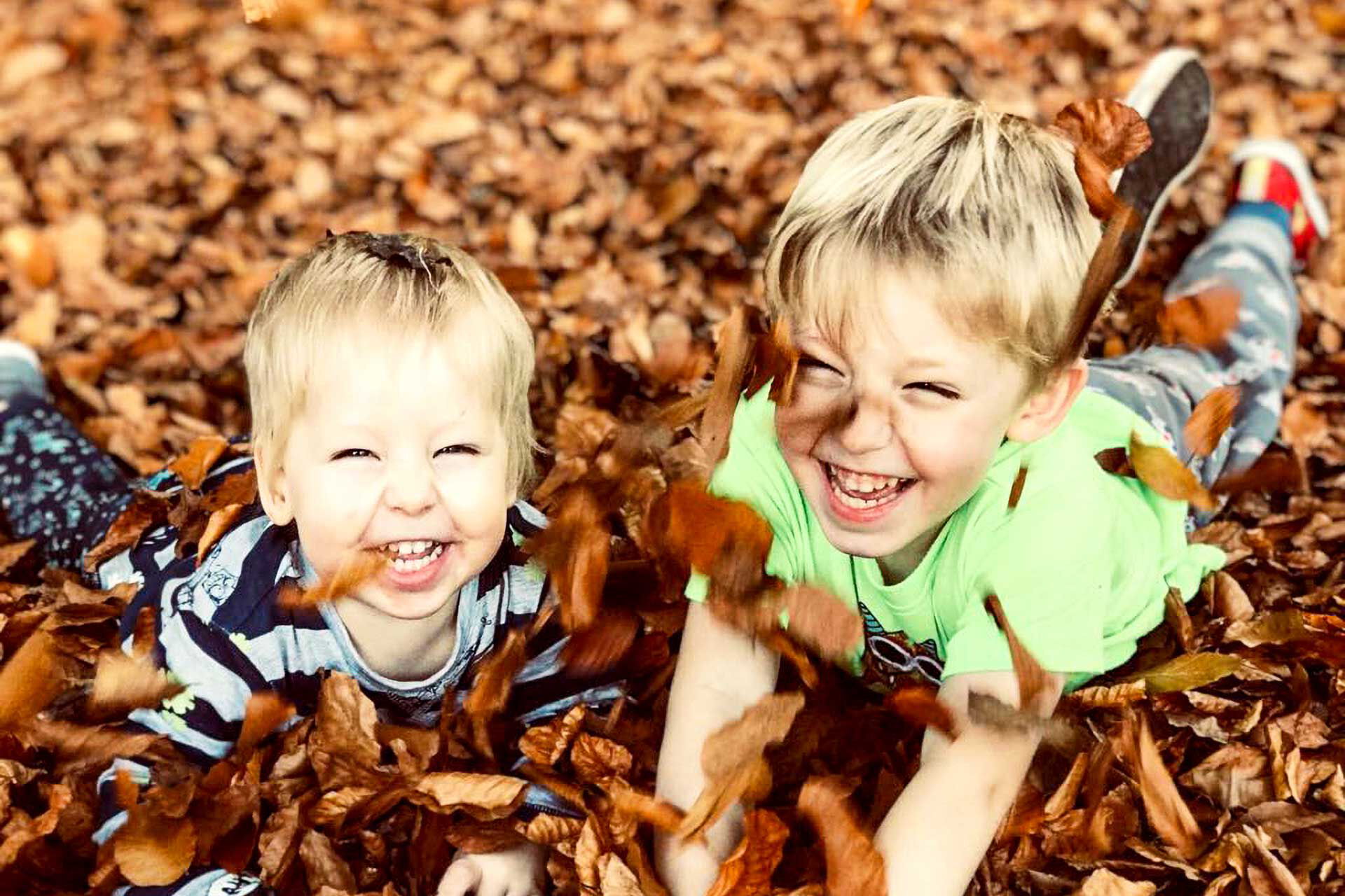 Zwei Kinder liegen lachend auf dem Waldboden im Laub.