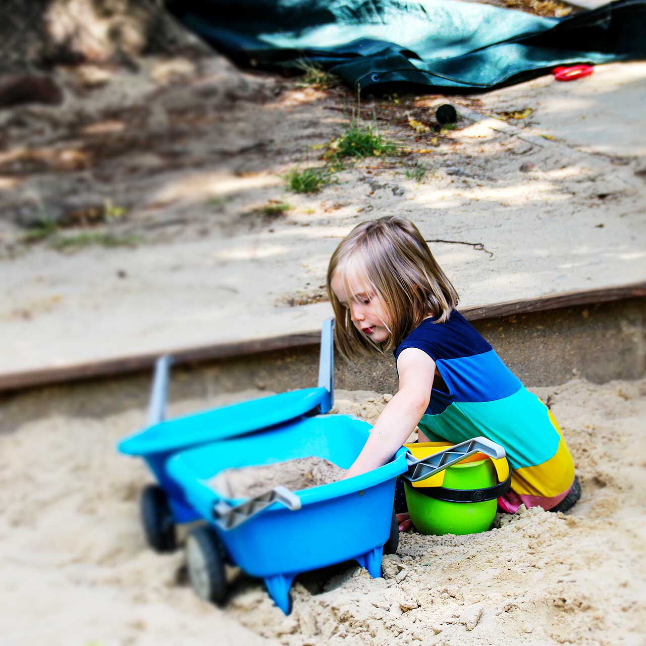 Ein Mädchen spielt mit einer Schubkarre im Sandkasten.