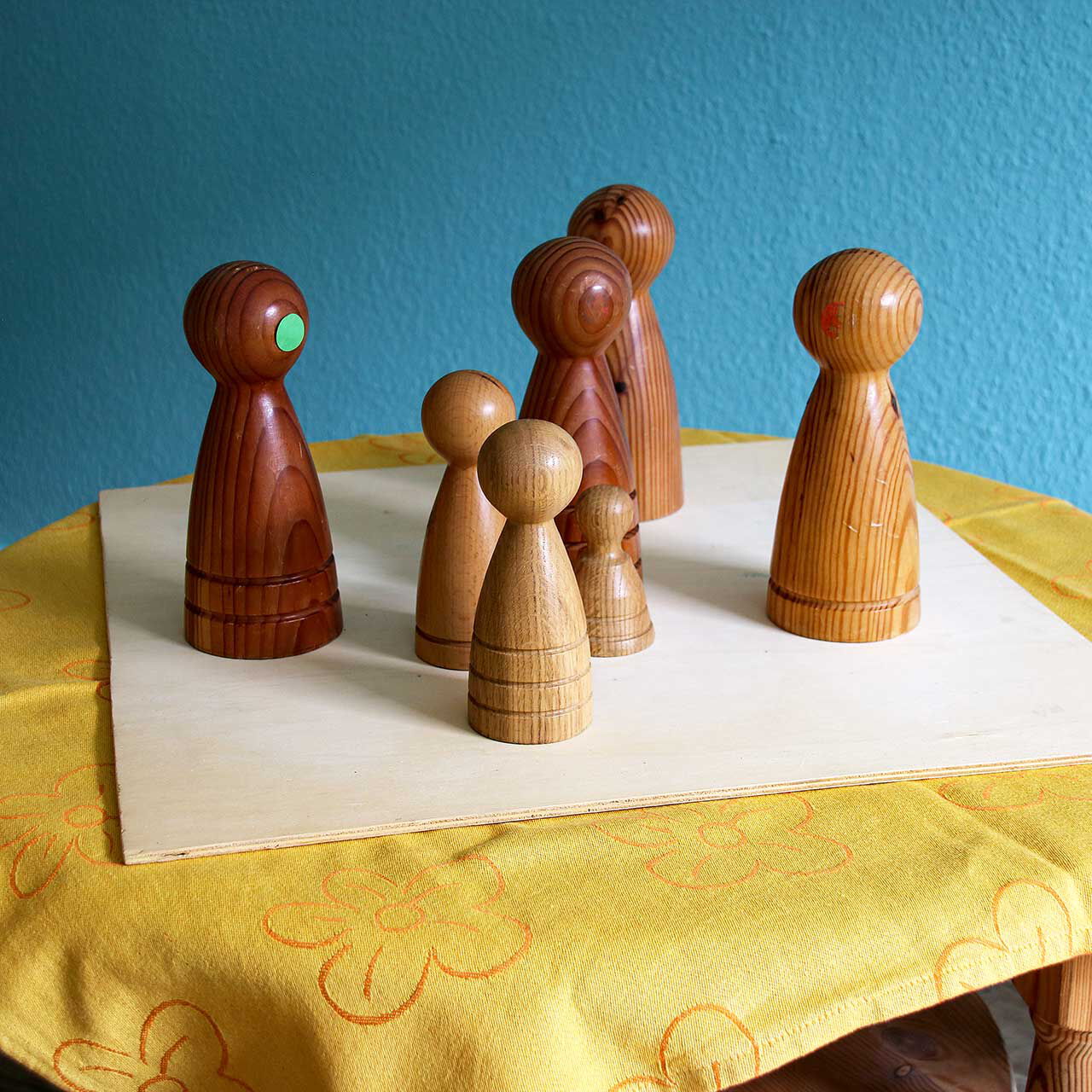7 Holzfiguren zur Personenaufstellung stehen auf einem Holzbrett auf dem Tisch.