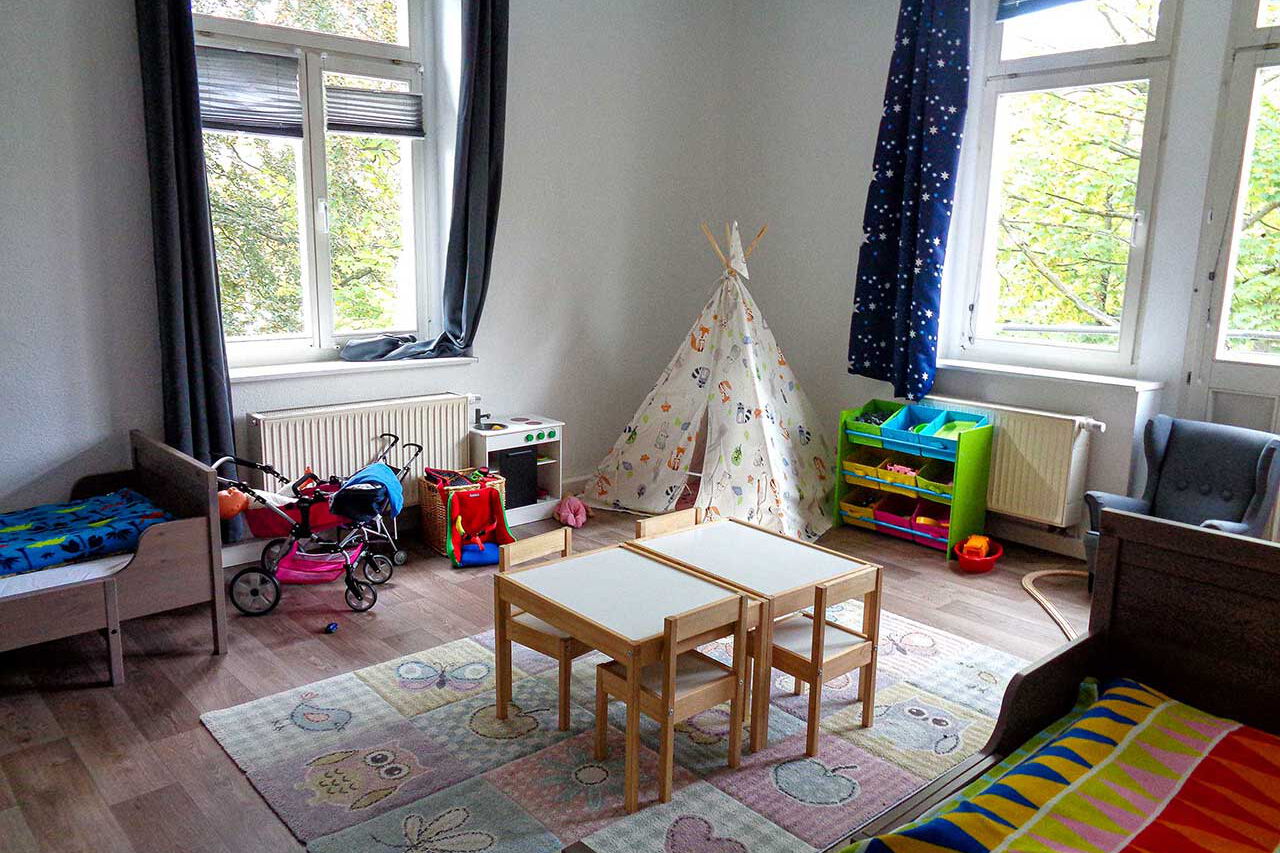 Der Spielbereich in einem Kinderzimmer mit einem Tipi, einer Kinderküche, zwei Kinderwagen und einem Kindertisch.