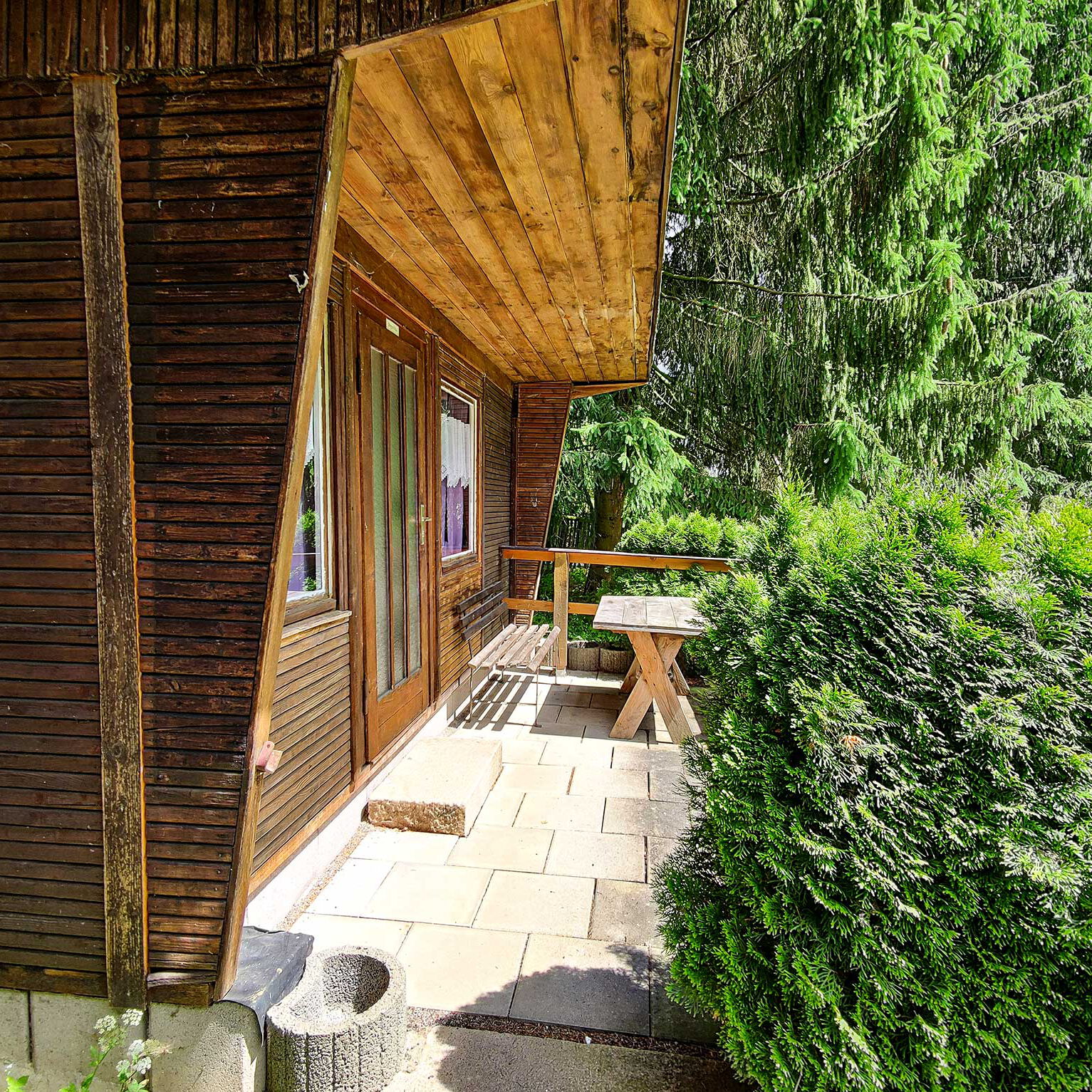 Eine Holzhütte mit zwei Schlafzimmern und jeweils einem Doppelstockbett. Vor der Doppelhütte ist eine kleine Terrasse mit einer Sitzmöglichkeit.