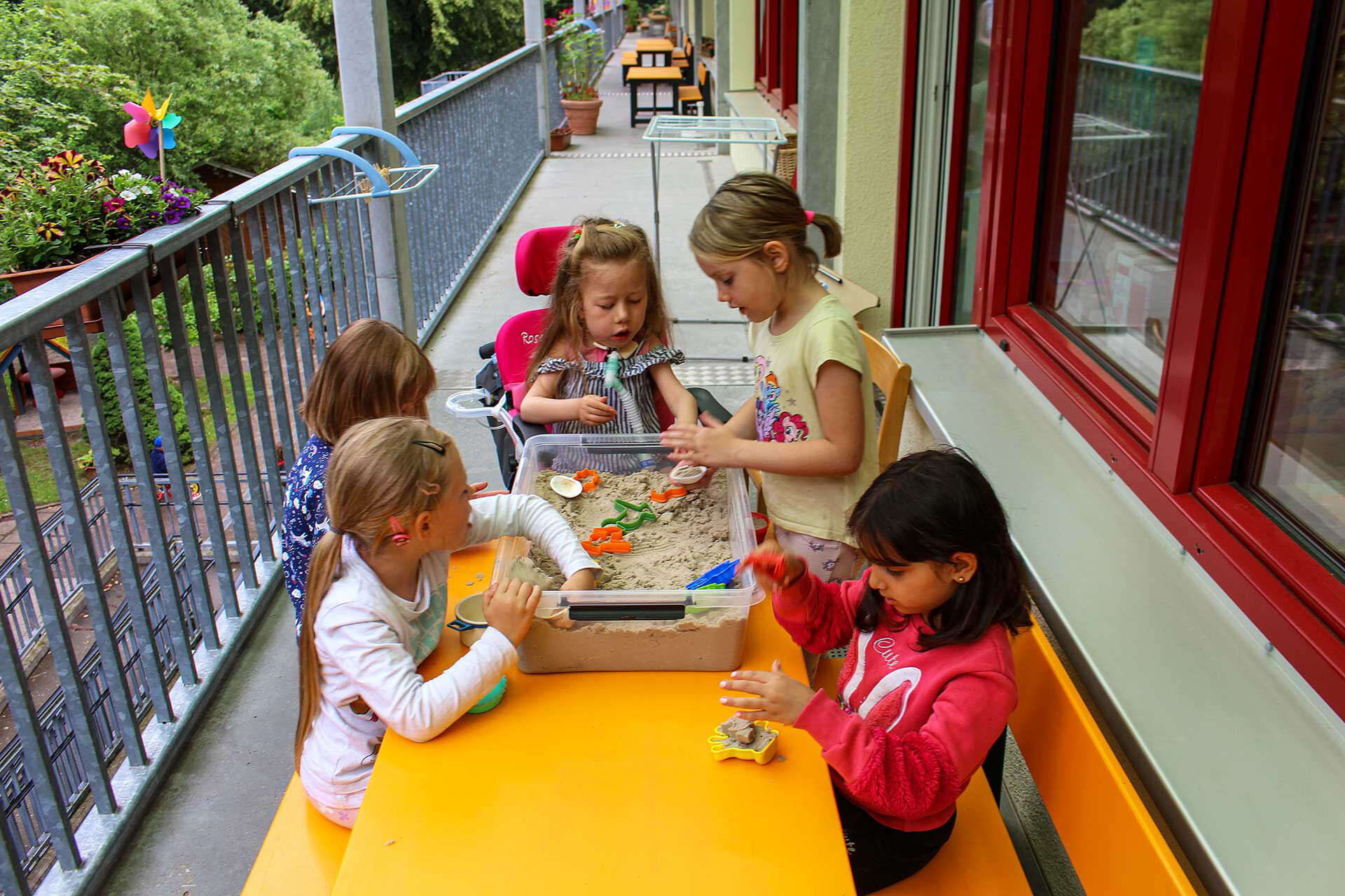 Fünf Kinder spielen in einer mit Sand befüllten großen Box auf der Terrasse der Einrichtung.