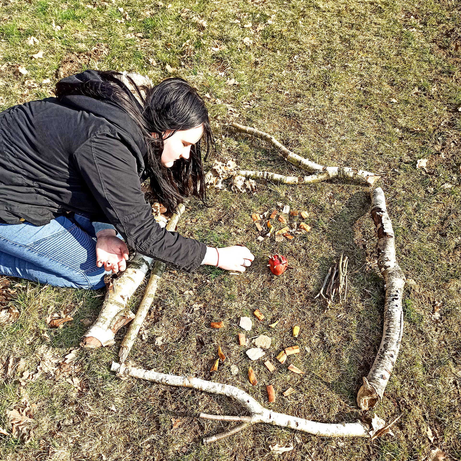 Eine junge Frau legt ein Bild aus Ästen, Kastanien und Stöcken.