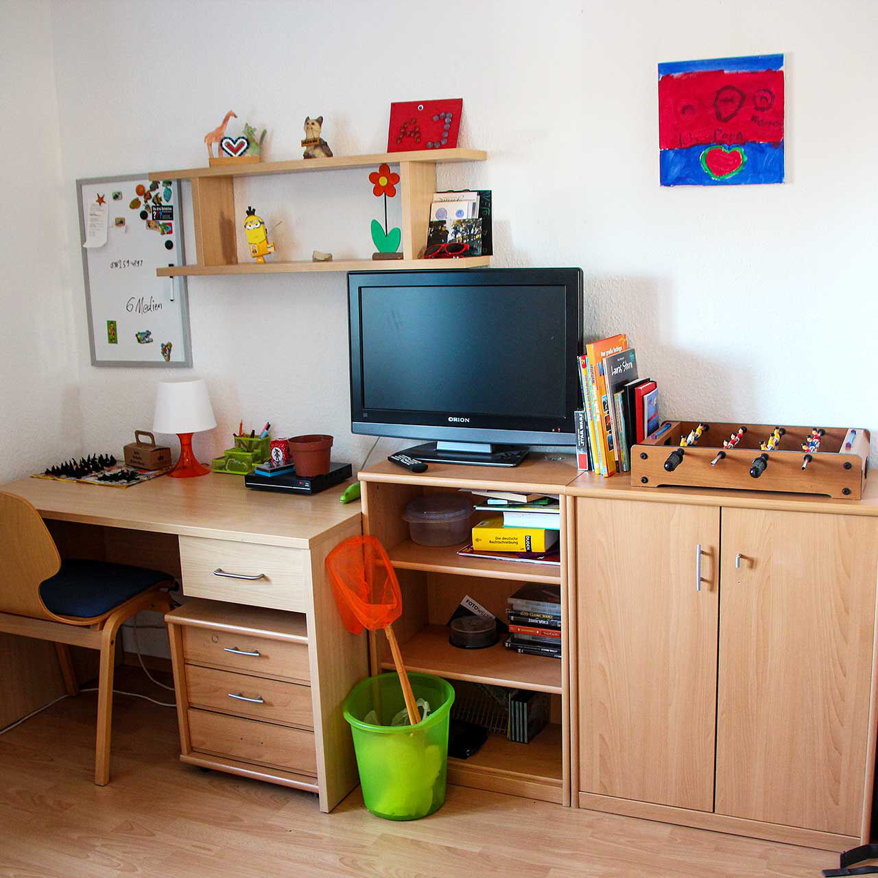 Ein Kinderzimmer mit einem Schreibtisch, Regal, einer Kommode und einem Fernseher.