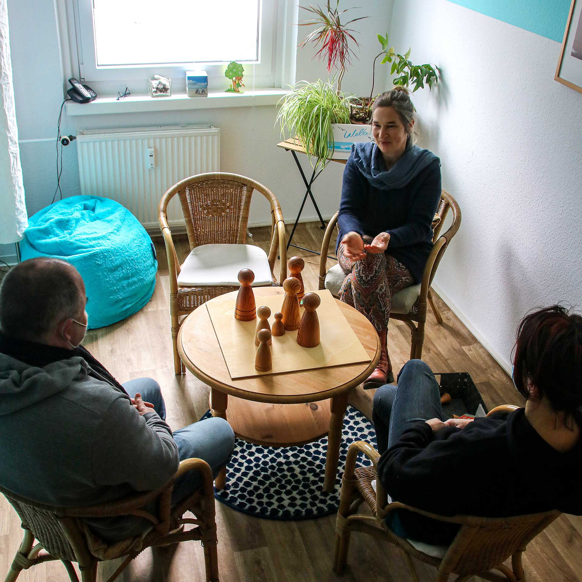 Ein Therapiegespräch von 3 Erwachsenen mit einer Personenaufstellung in Form von Holzfiguren.