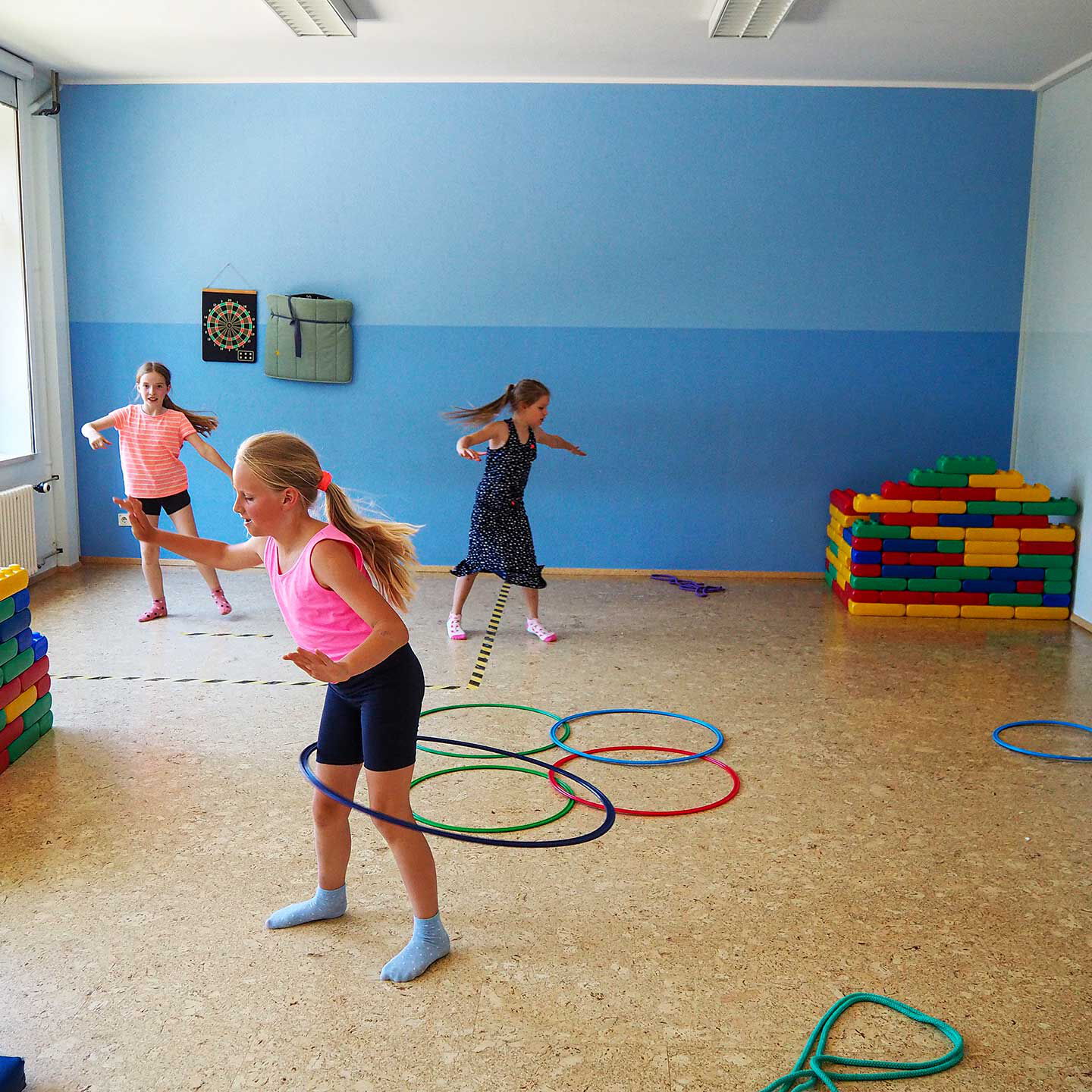 Das Sportzimmer mit einem Boxsack, Bausteinen, Seilen und Reifen. Es spielen drei Mädchen im Sportzimmer.