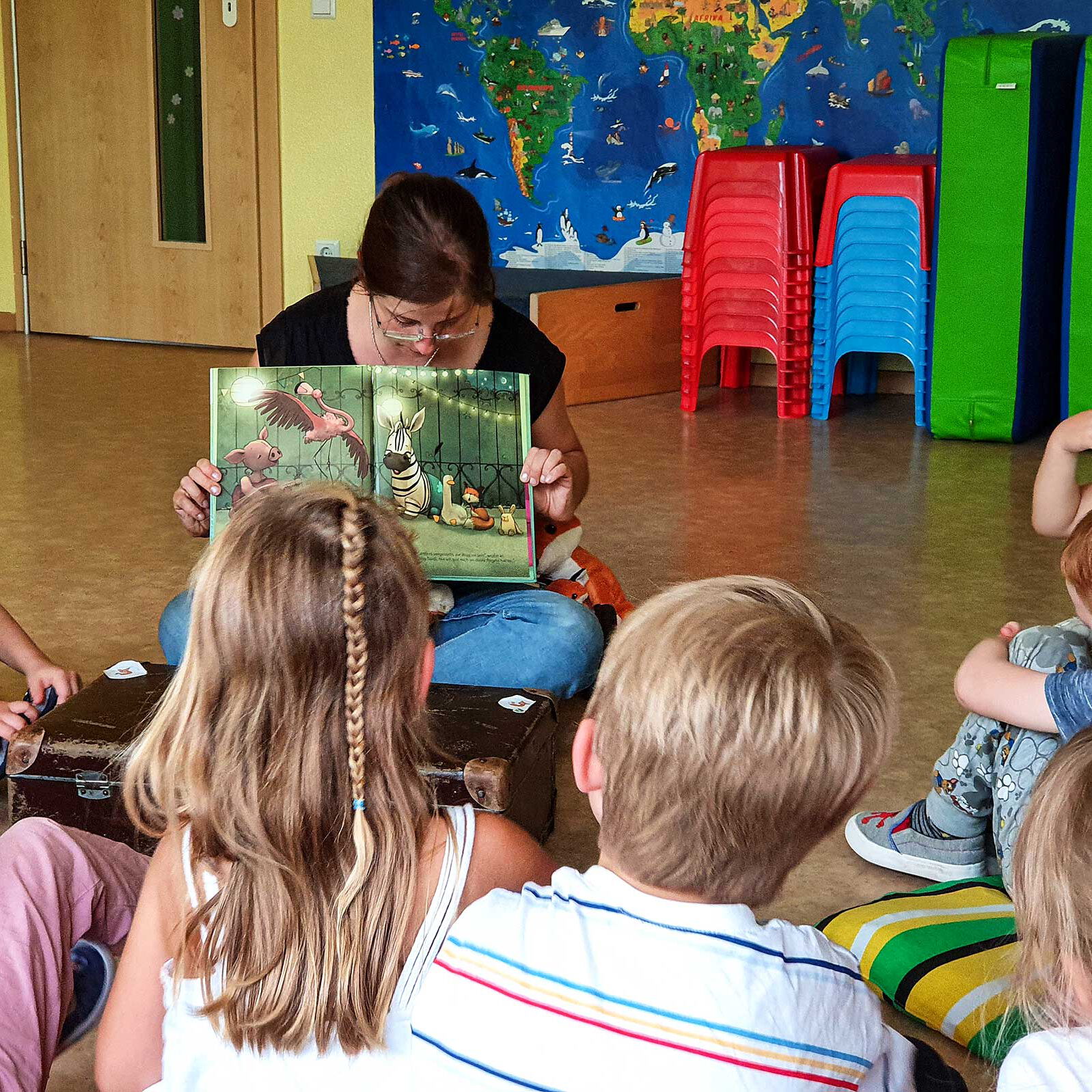 Eine Gruppe von Kindern sitzt auf dem Boden und die Vorlesepatin liest ihnen ein Buch vor.