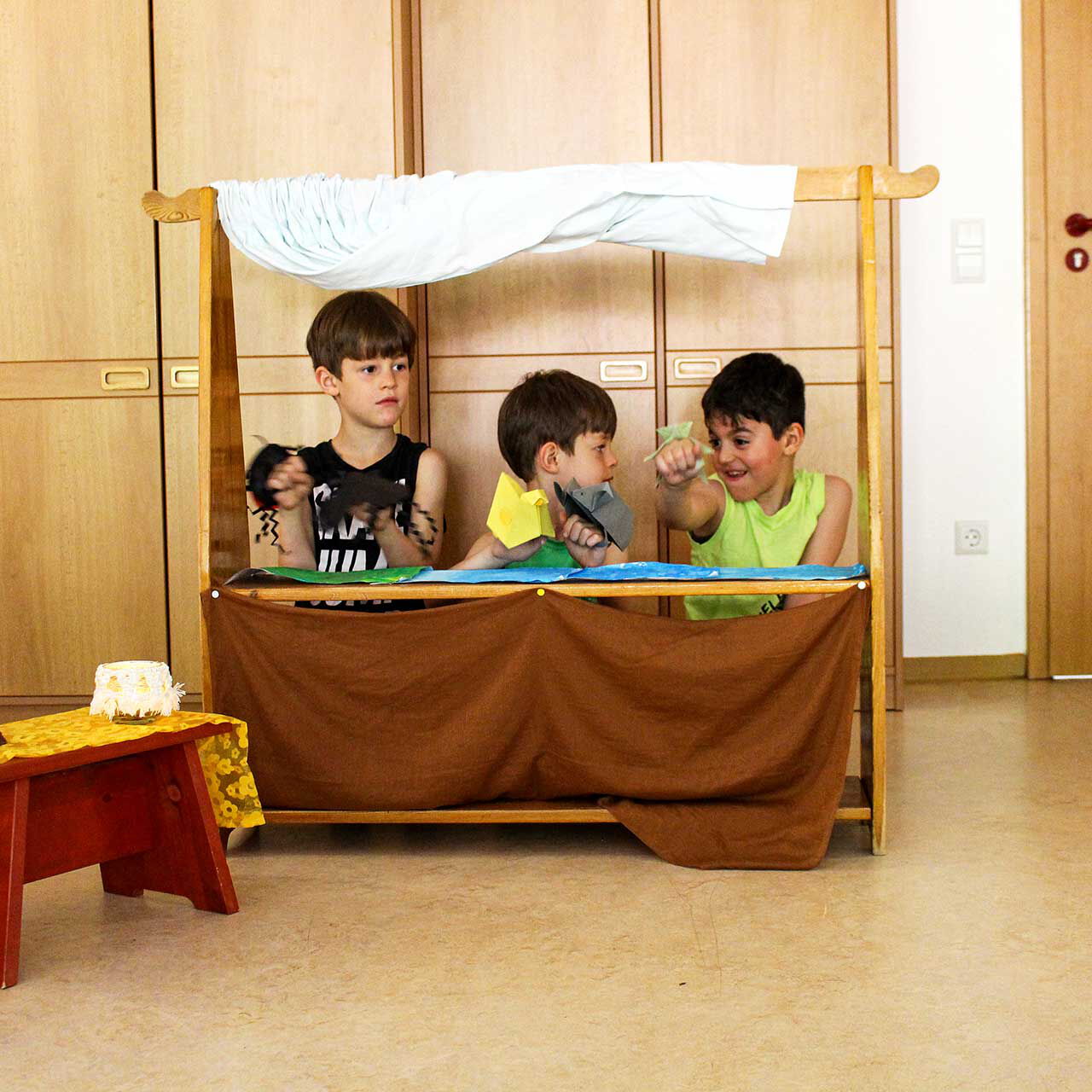 Drei Jungs spielen mit einem Puppentheater und haben selber Papierfiguren gebastelt.