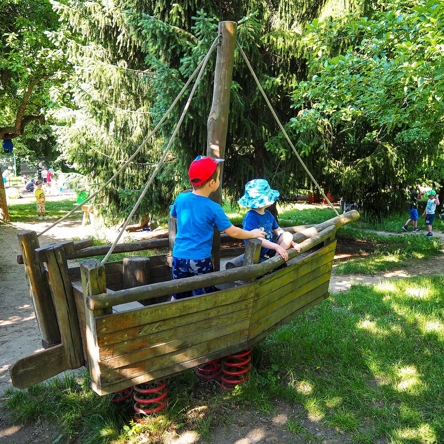 Auf einem Holzschiff im Gartenbereich spielen zwei Kleinkinder.