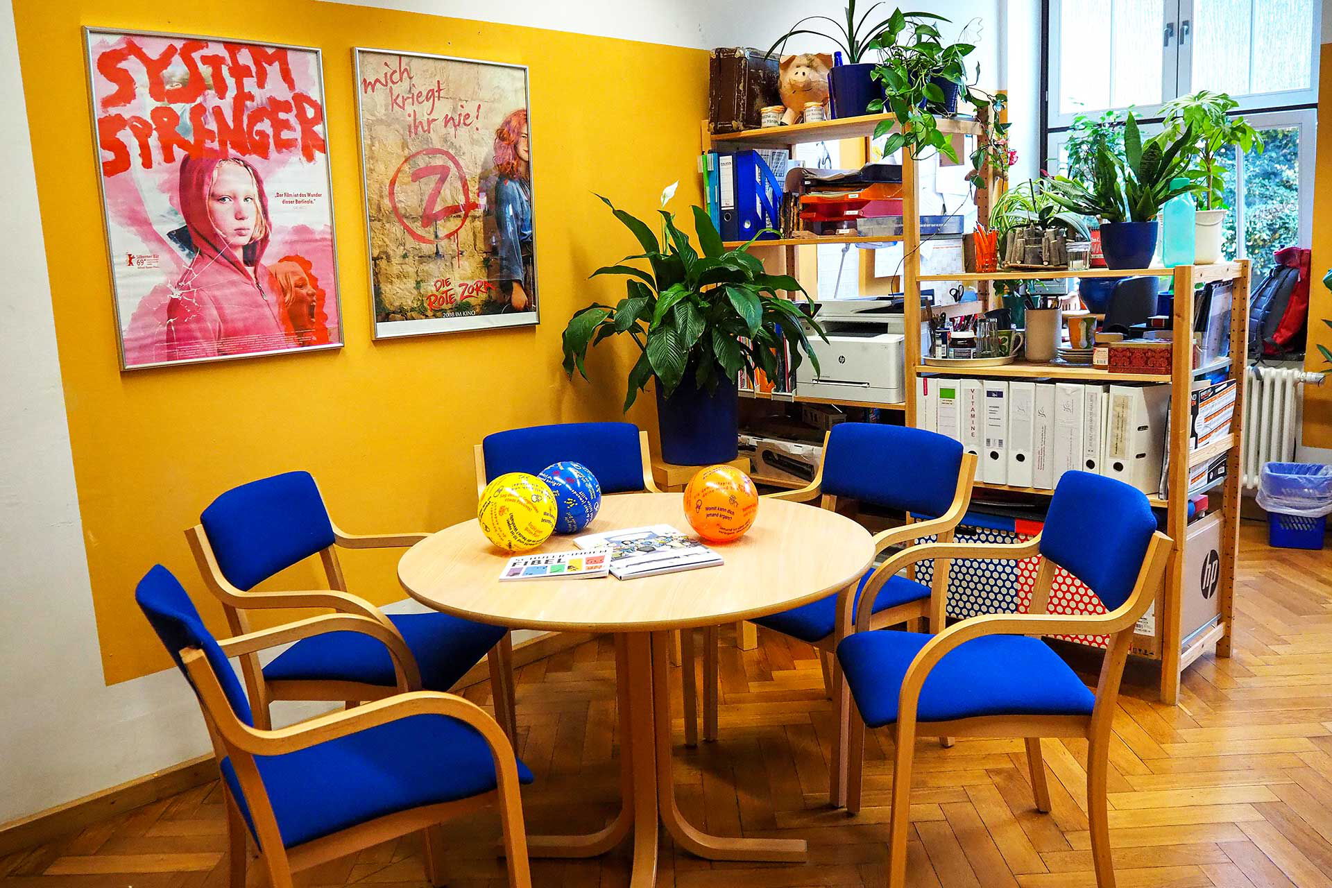 Das Büro der Schulsozialarbeit mit einem Beratungstisch, fünf Stühlen und im Hintergrund ein Arbeitsbereich mit Drucker und PC.