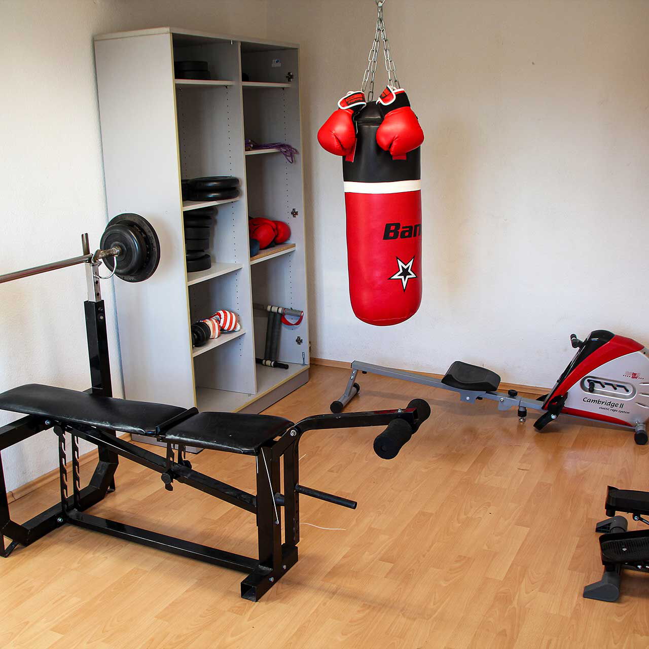 Der Sport- und Fitnessraum mit einem Boxsack, Rudergerät, Stepper und Krafttrainingsgerät.
