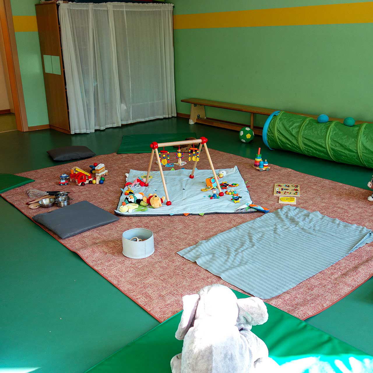 In Vorbereitung auf die Krabbelgruppe sind Decken auf dem Boden, Spielsachen und Matten verteilt.