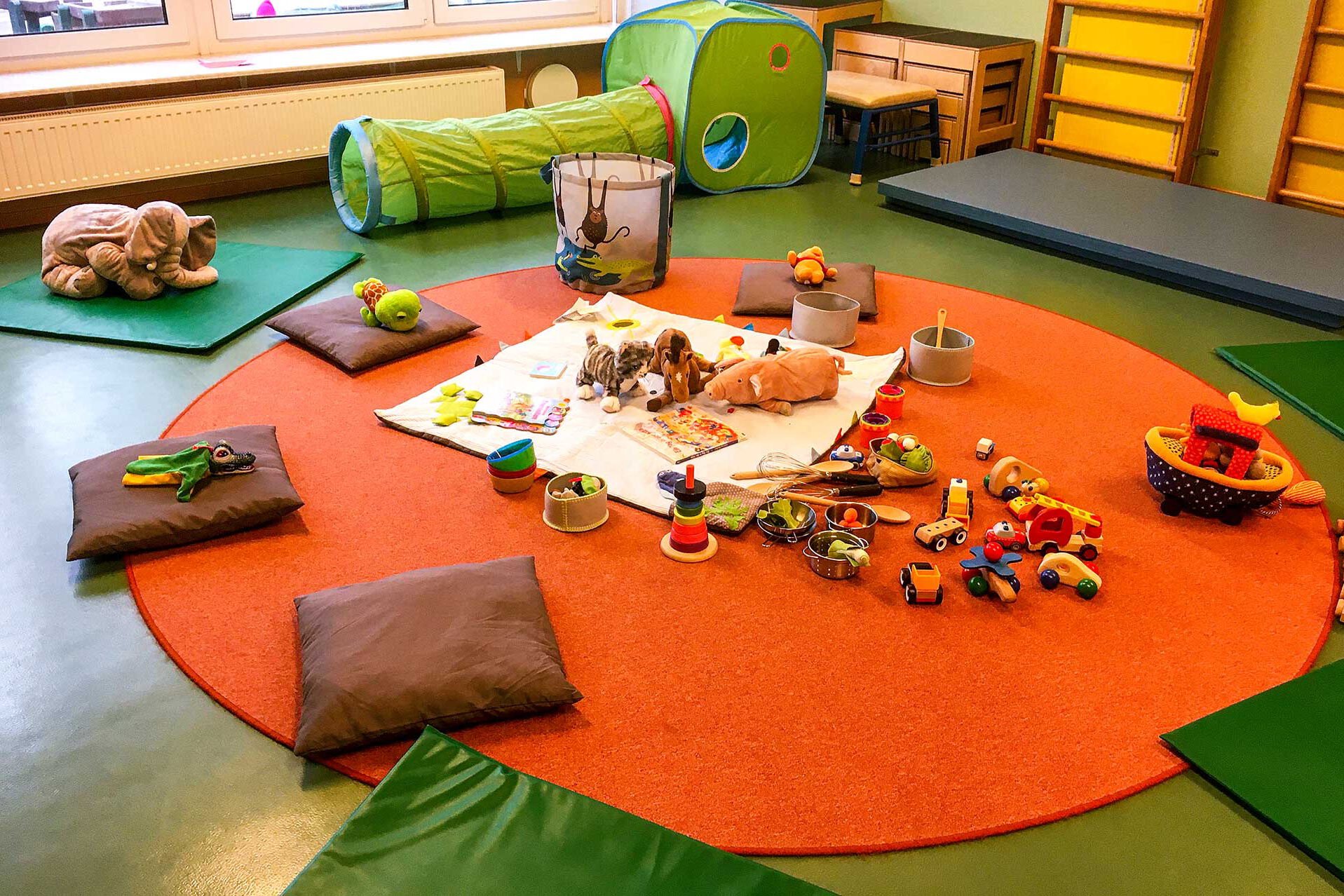 Zur Spielstunde sind auf dem Fußboden im Spielzimmer Decken und Matten mit viel Spielzeug ausgebreitet.