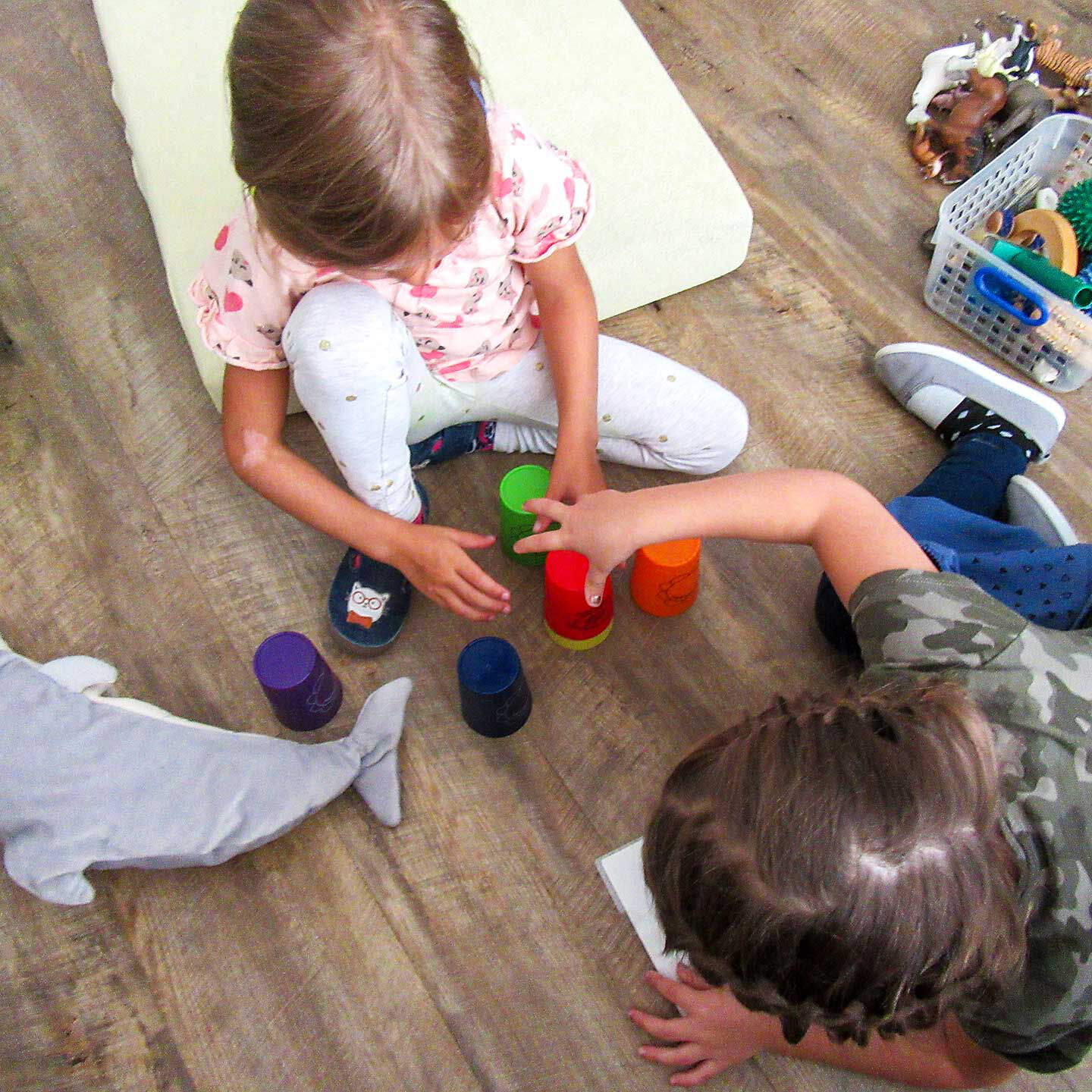 Zwei Kinder sitzen auf dem Fußboden und spielen mit den Stapelbechern.