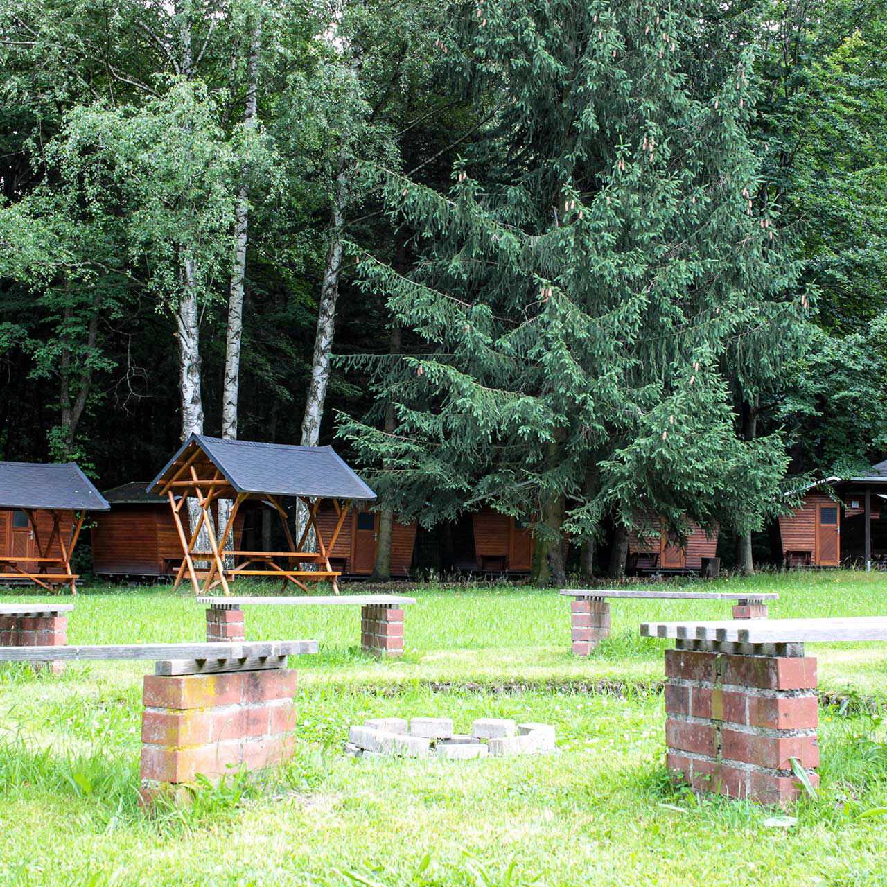 Der Lagerfeuerplatz mit festen Sitzbänken und im Hintergrund stehen die Holzhäuschen.