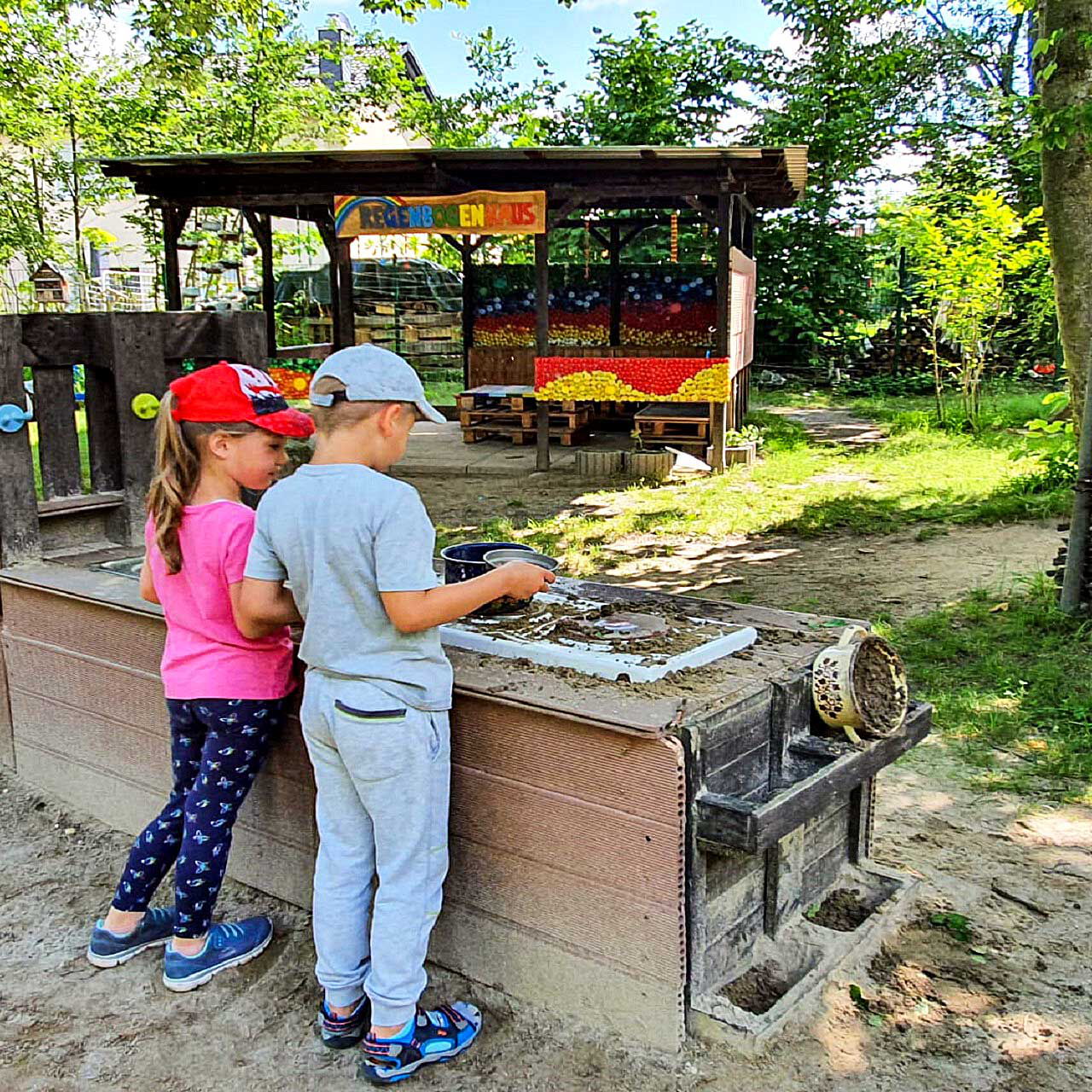 In der Outdoorküche spielen zwei Kinder zusammen am Herd mit Sand.