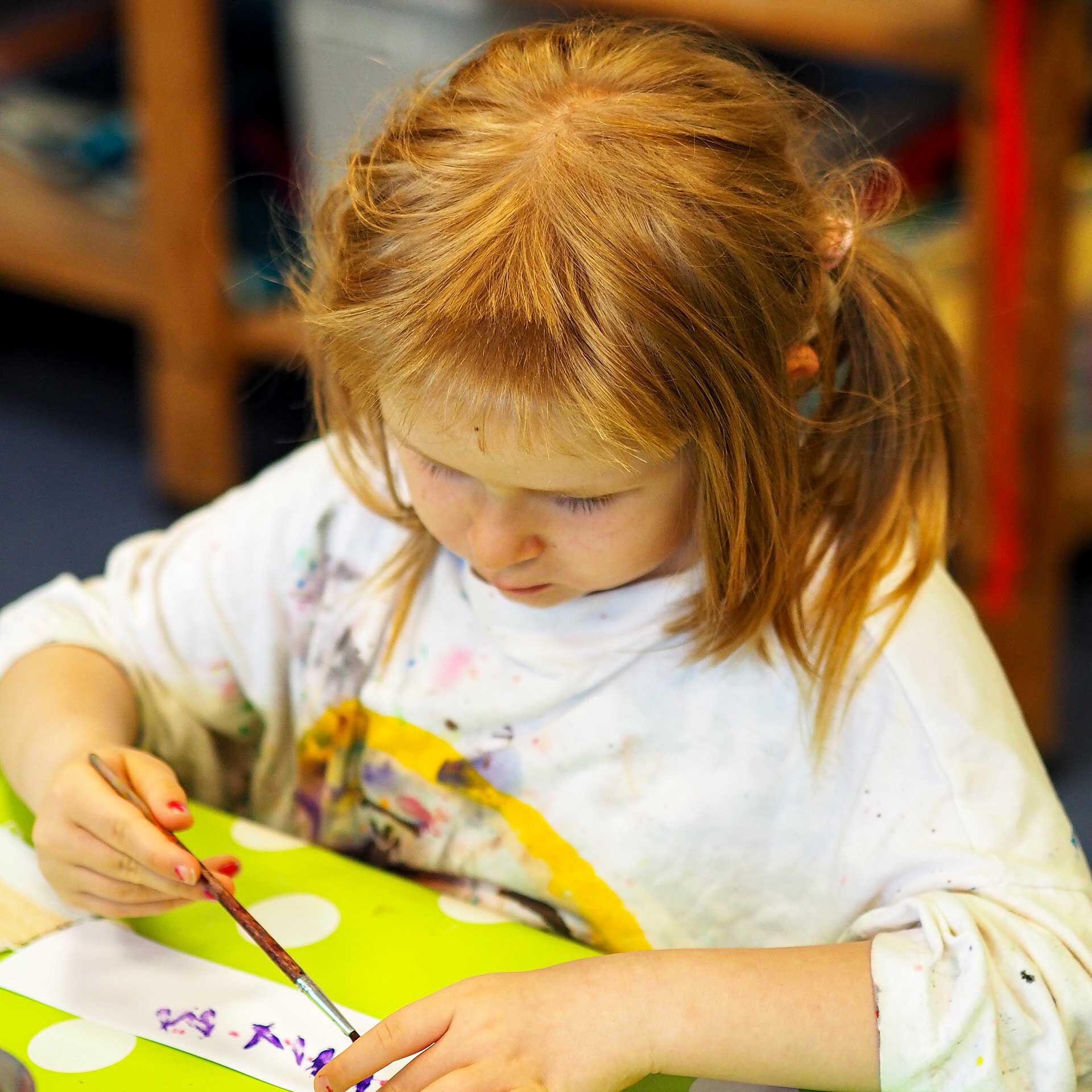 Im Atelier malt ein Mädchen mit lila Farbe auf ein Stück Papier.