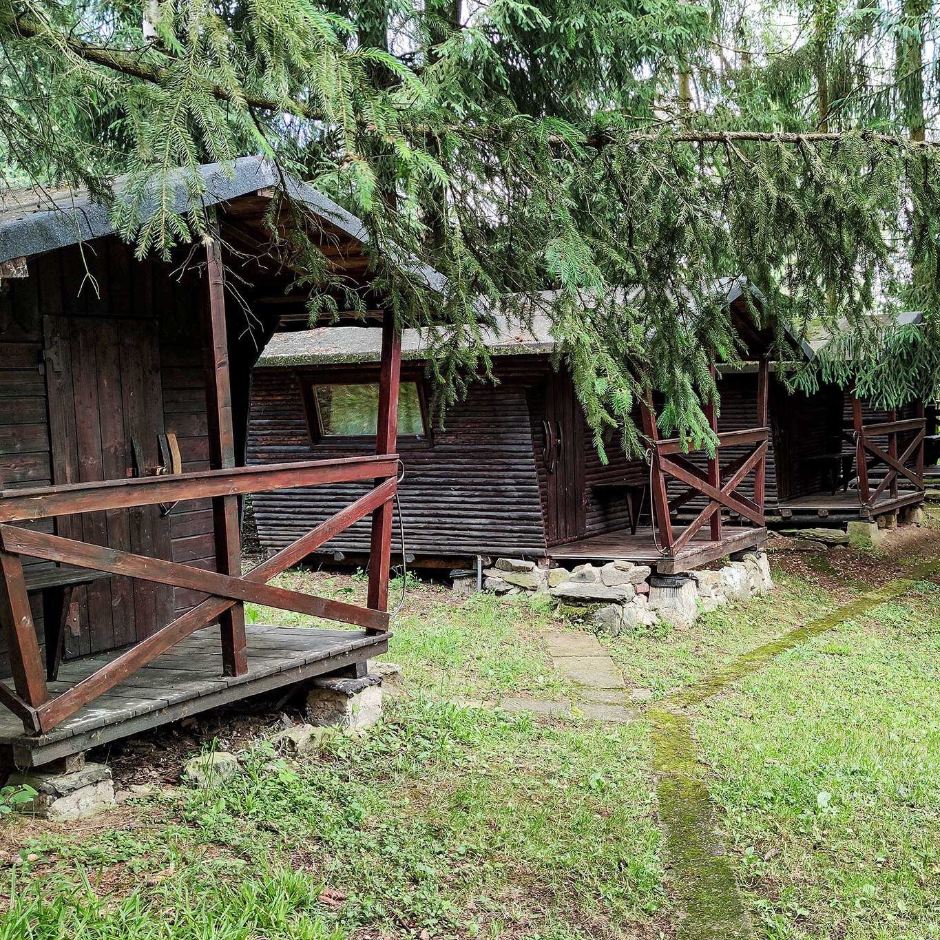 Vier Holzblockhütten nebeneinander mit jeweils einer kleinen Terrasse.