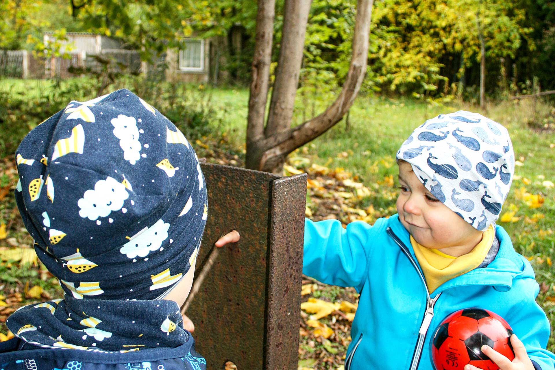 Zwei Kinder spielen im Freien auf einer Wiese an einem Baum.