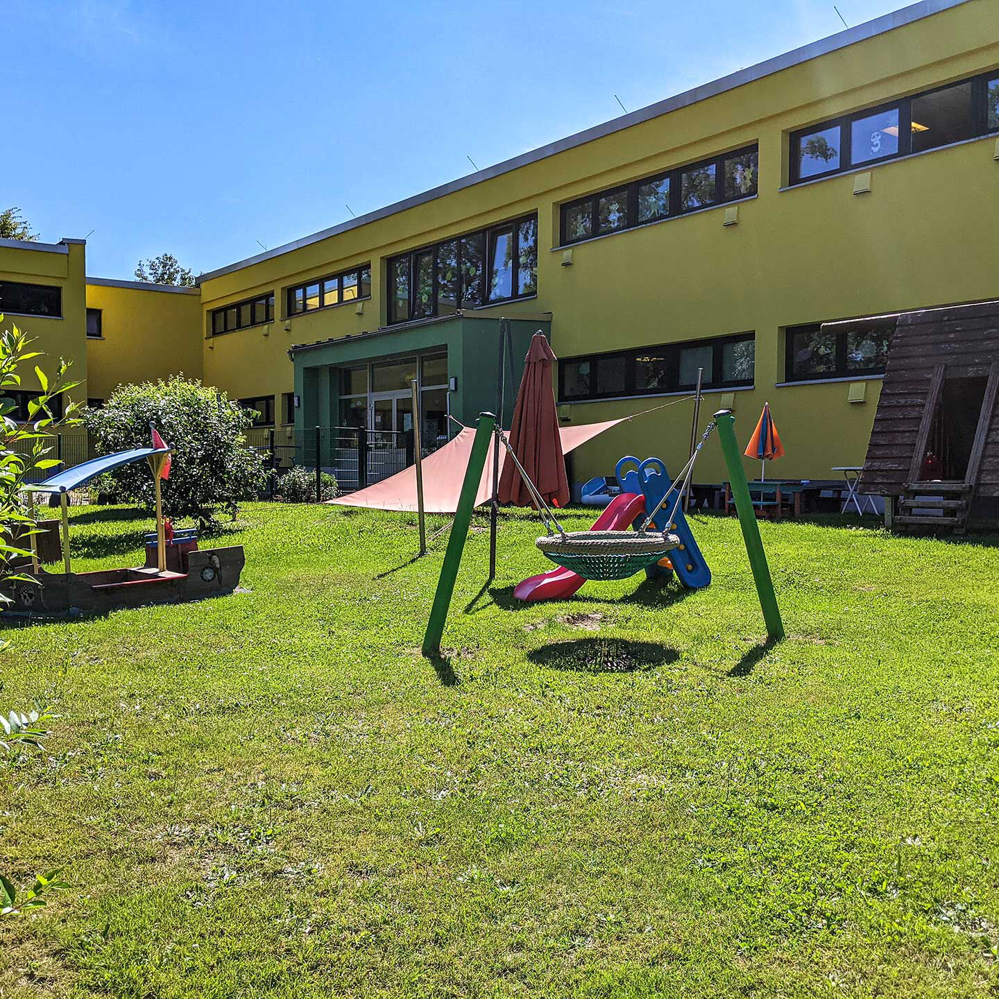 Der Kleinstkindgarten am Standort Bernhardstraße 77 mit einer Nestschaukel, überdachtem Sandkasten und einer Rutsche.