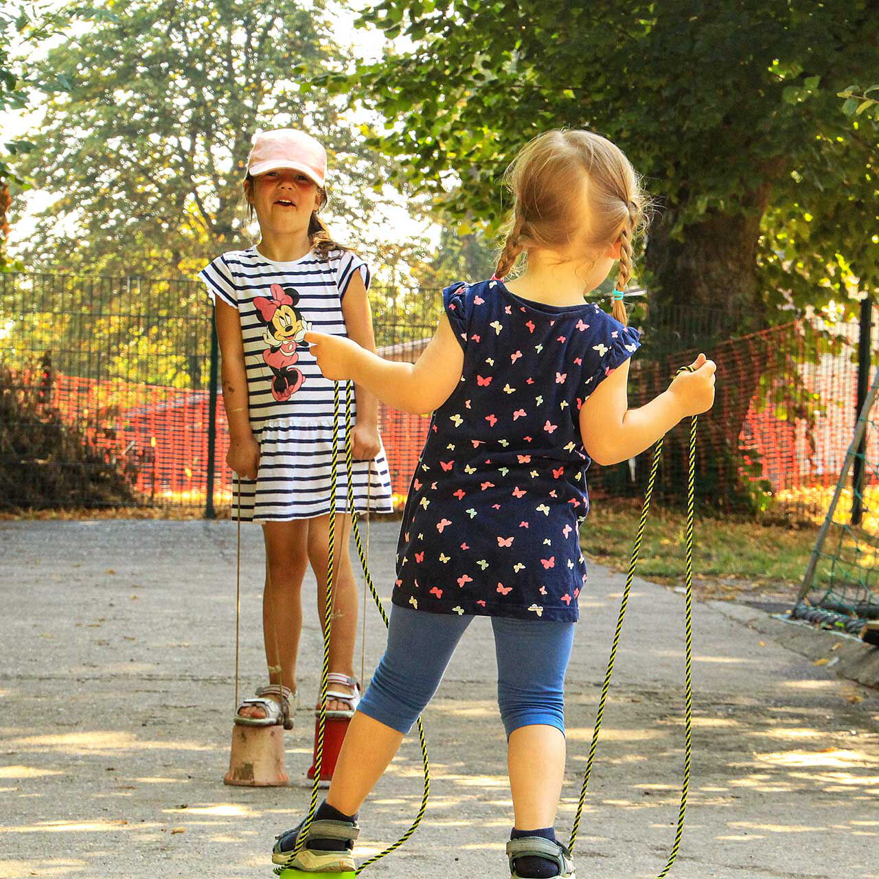 Zwei Kinder balancieren und spazieren auf Laufdosen im Außengelände.