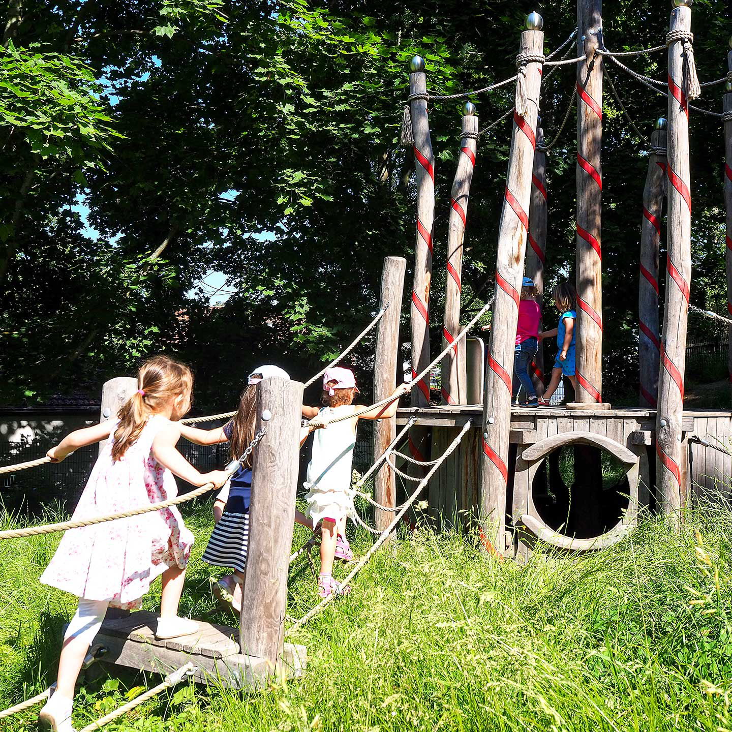 Auf dem Kletterbaum aus Holz spielen und klettern fünf Kleinkinder.