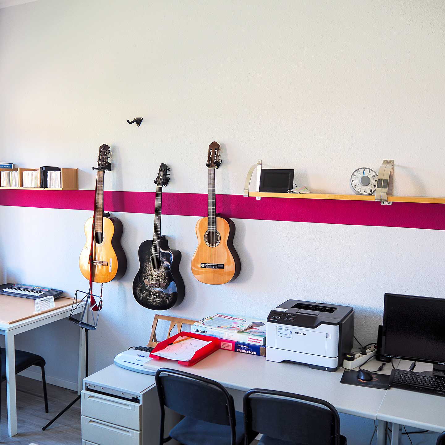 Im Kreativzimmer hängen drei Gitarren an der Wand, ein kleines Keyboard steht auf einem Tisch in der Ecke und ein Computer steht zur Benutzung auf einem Schreibtisch im Bildvordergrund.