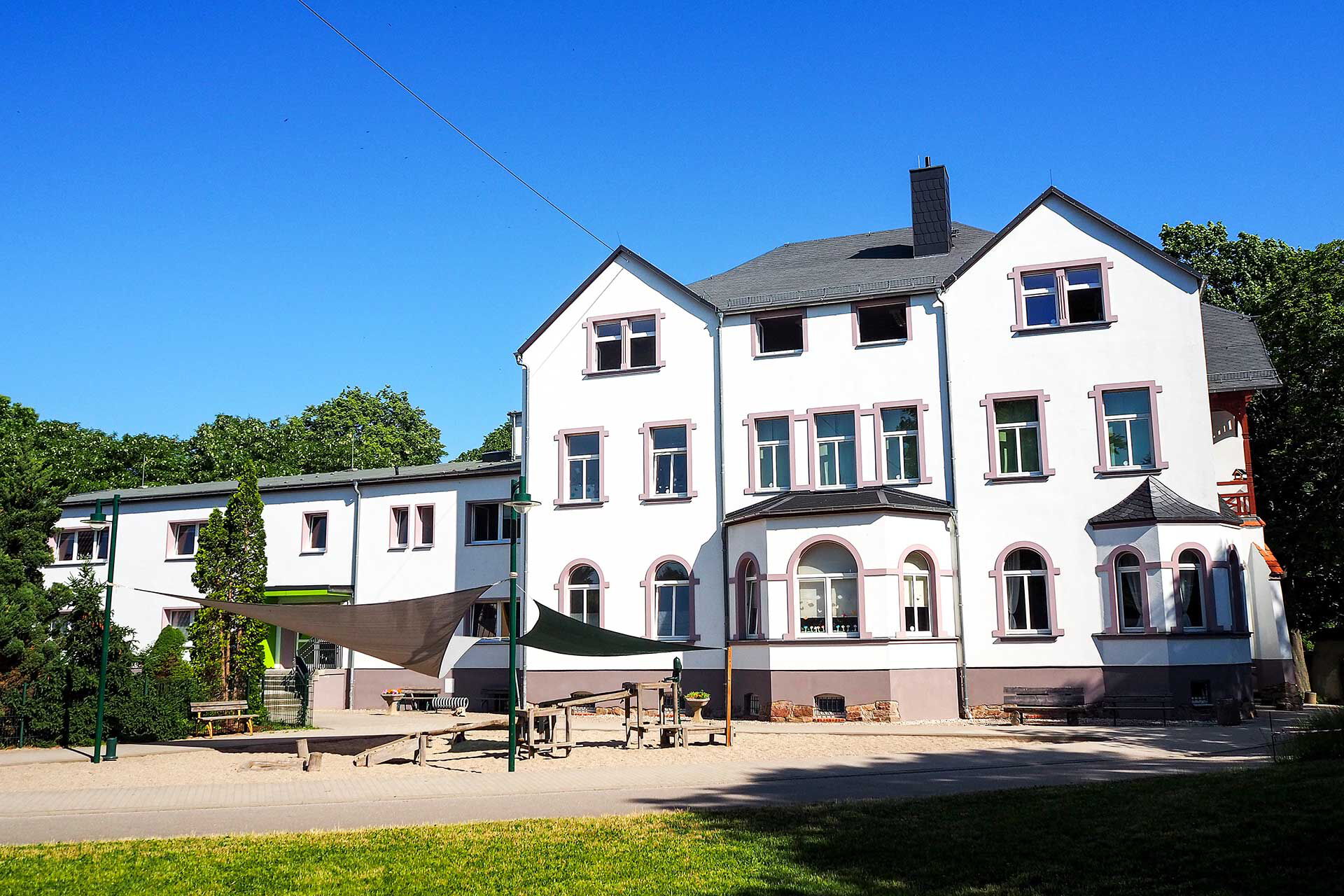 Das Hauptgebäude Haus Floh mit der Matschanlage im Bildvordergrund.