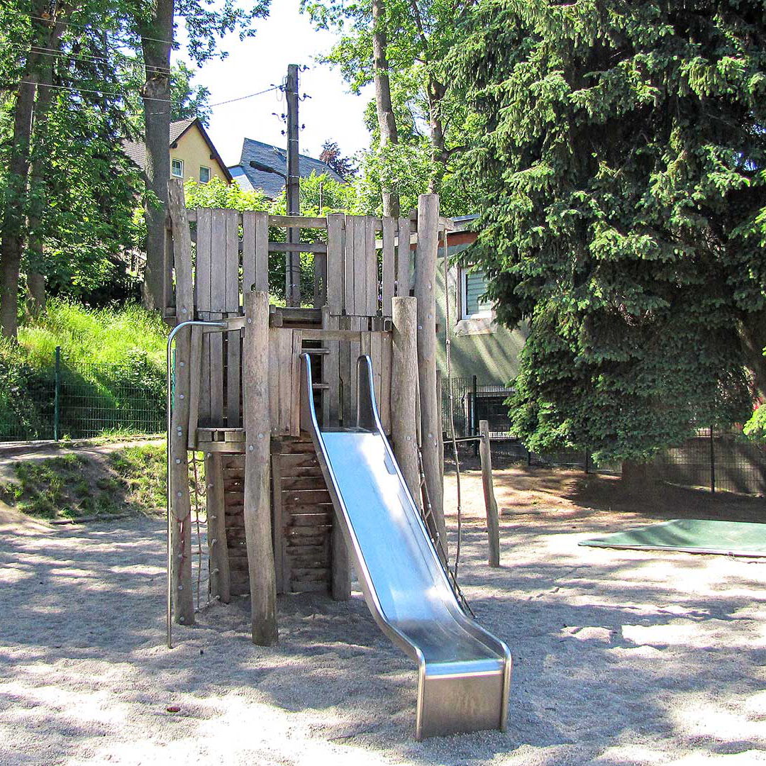 Ein Spielturm aus Holz mit einer Rutsche und Klettergerüst im Außenbereich.