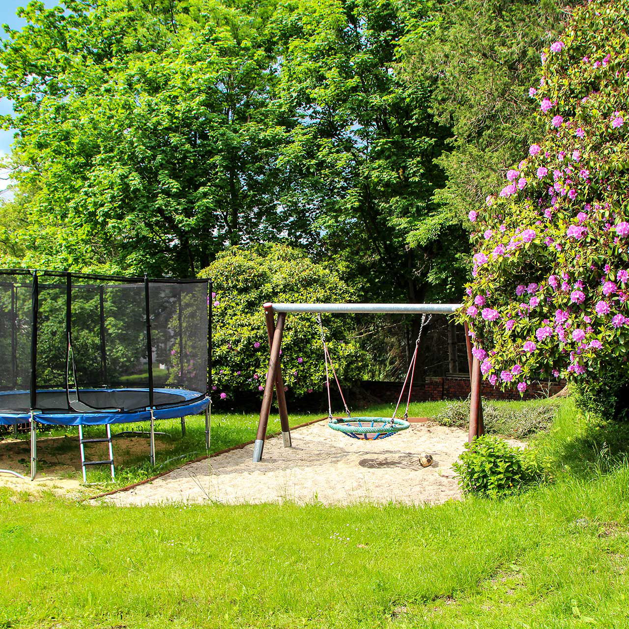 Das Außengelände mit einem großen Trampolin und einer Nestschaukel.