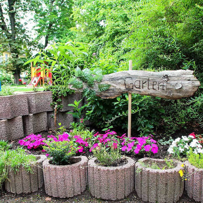 In einem Blumenbeet steht ein Wegweiser zum Garten.