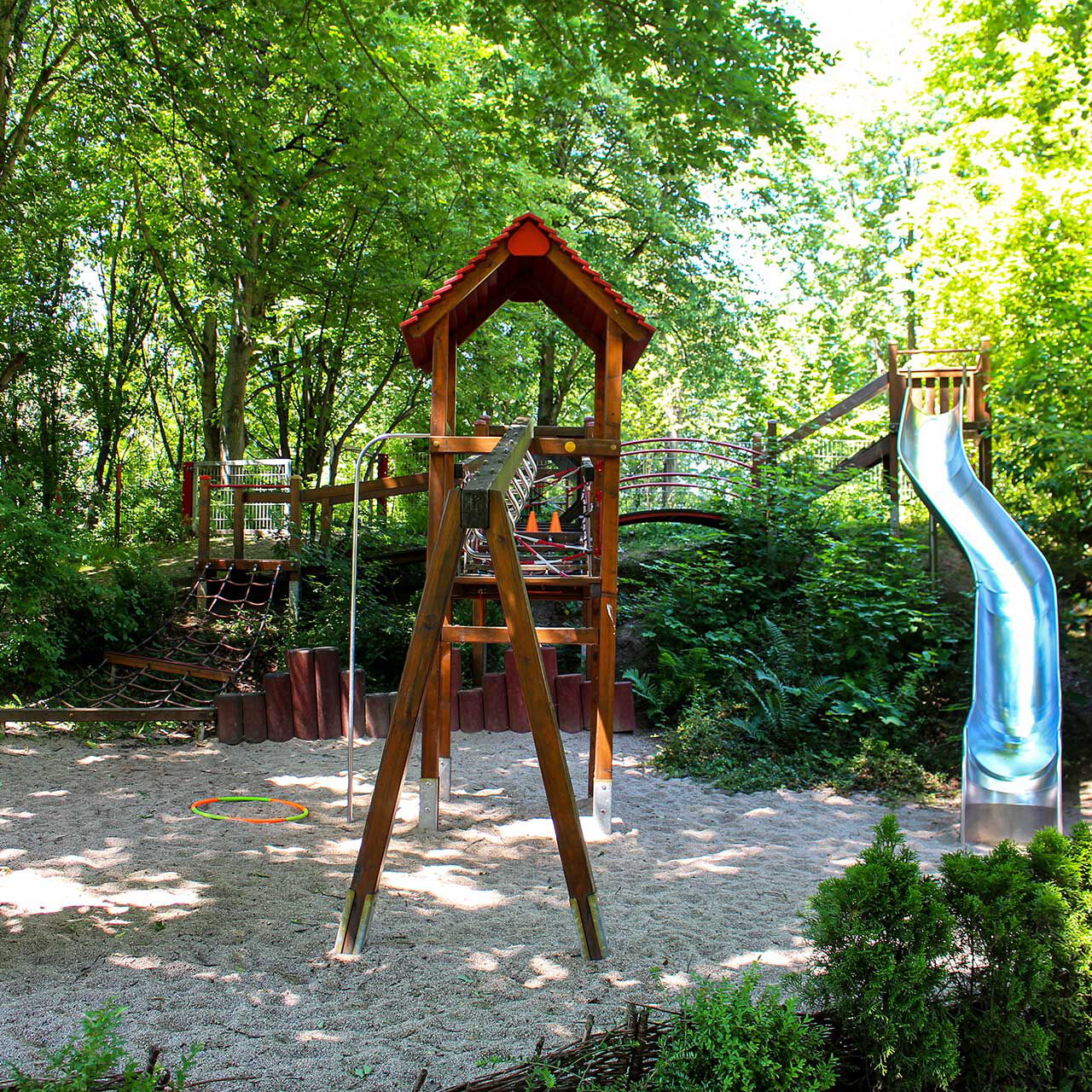 Ein Spielplatz im Außengelände mit einer großen Rutsch und unterschiedlichen Spiel- und Klettergeräten aus Holz.