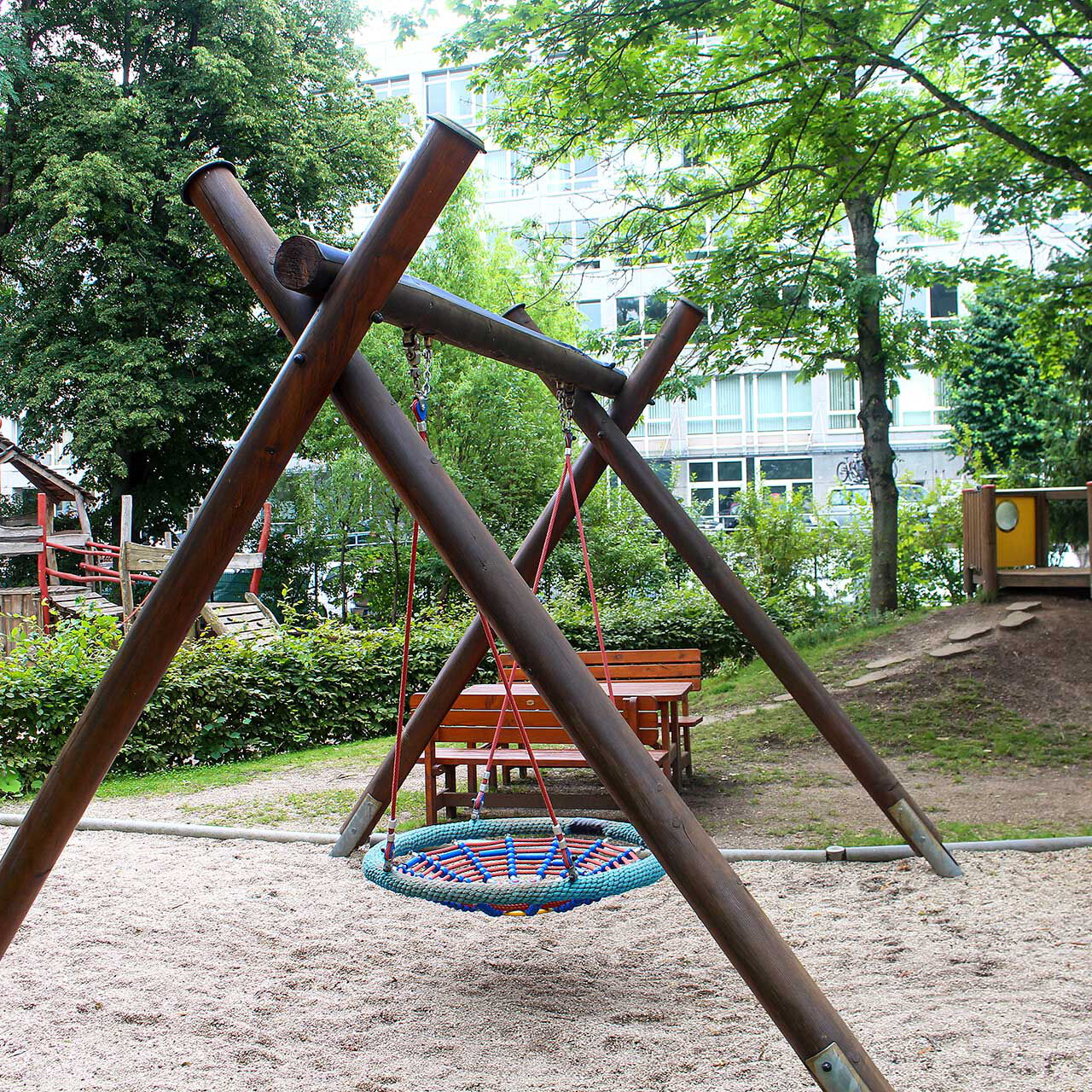 Eine Nestschaukel im Außenbereich. Im Hintergrund steht der Kletterturm.