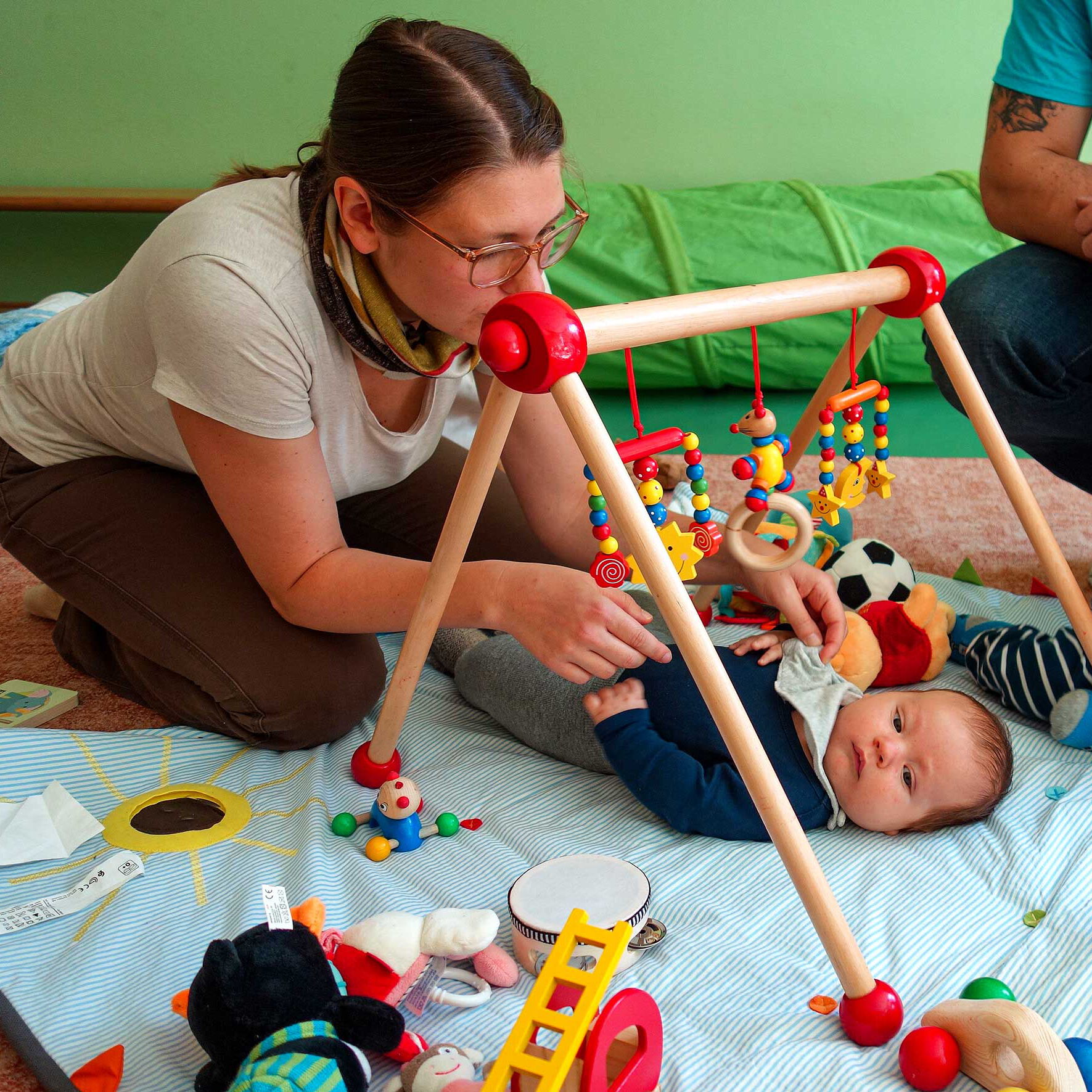 Ein Baby liegt rücklinks auf einer Decke und davor kniet die Kindesmutter.