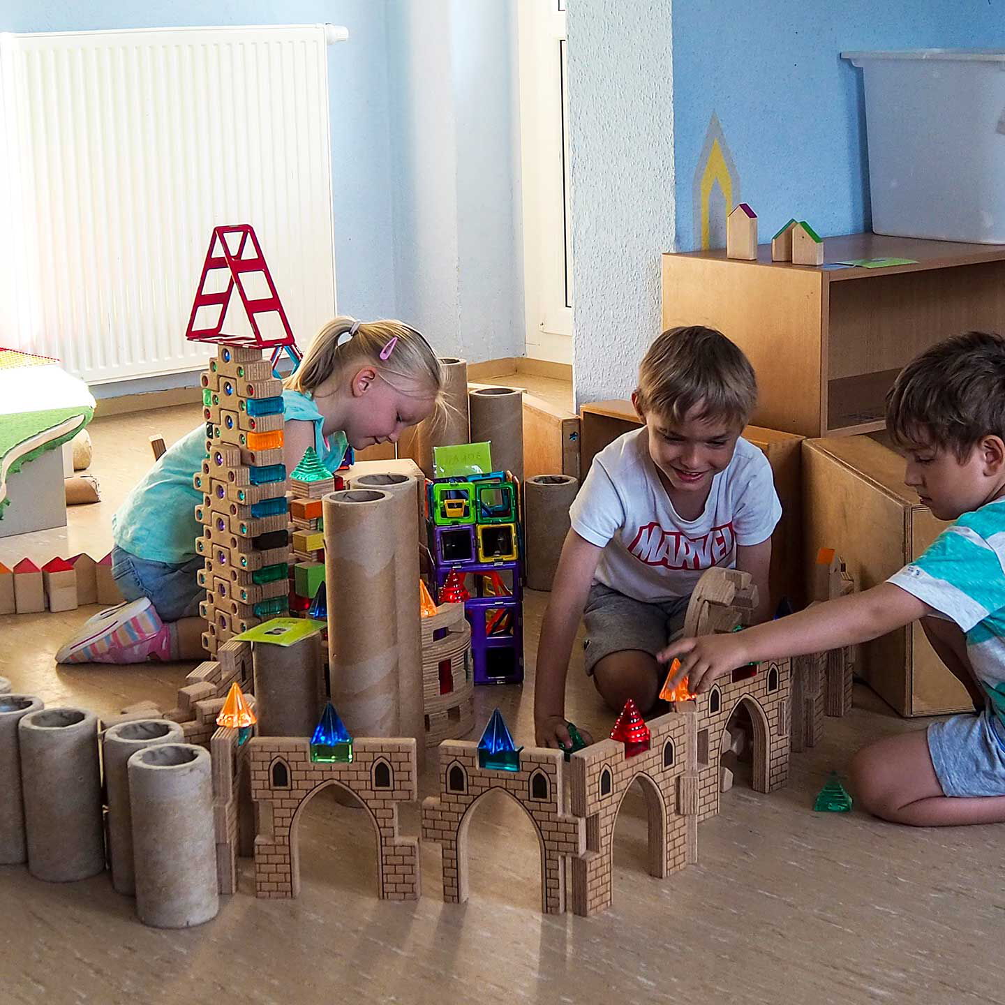 Im Bauzimmer spielen drei Kinder mit Bausteinen und haben viele Türme und Zäune aufgebaut.