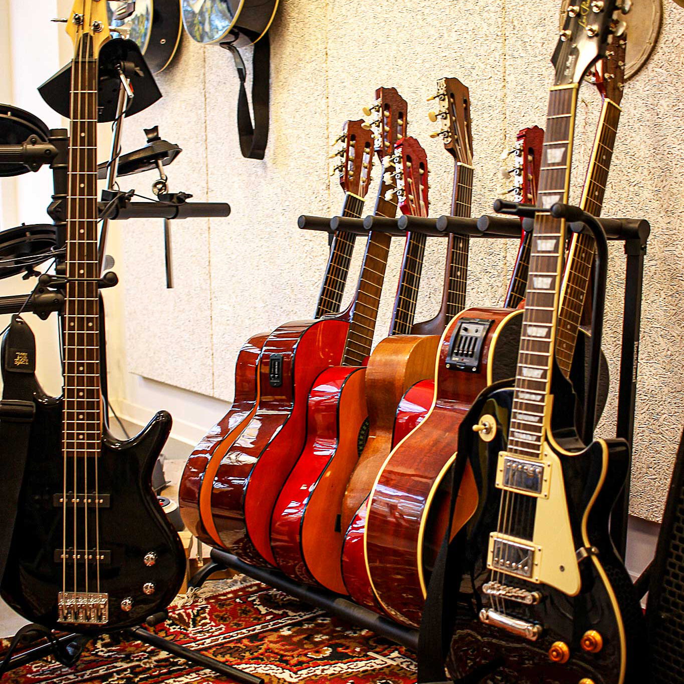 Es stehen acht Gitarren im Vordergrund und an der Wand im Hintergrund hängen nochmals drei Gitarren.