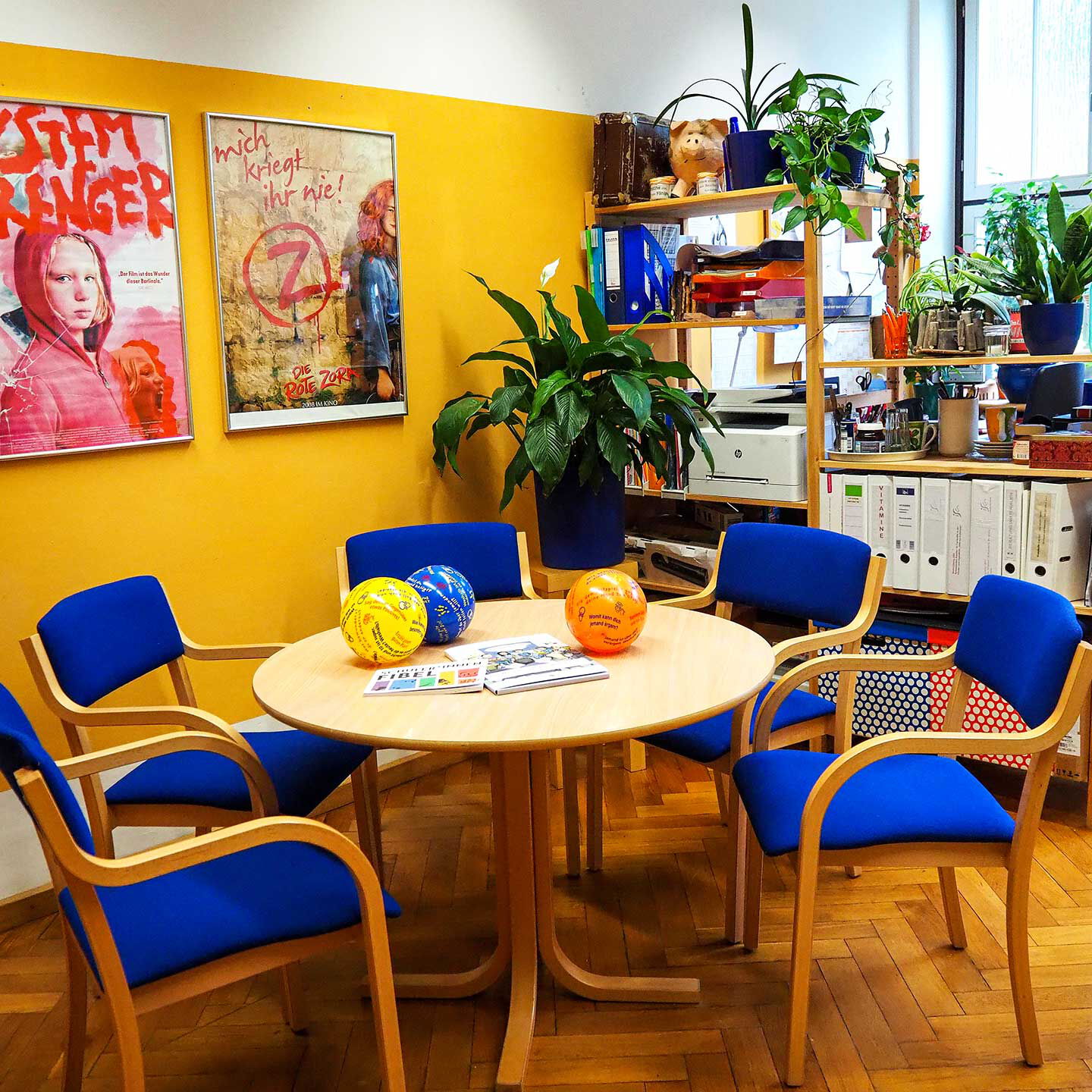 Das Büro der Schulsozialarbeit mit einem Beratungstisch, fünf Stühlen und im Hintergrund ein Arbeitsbereich mit Drucker und PC.