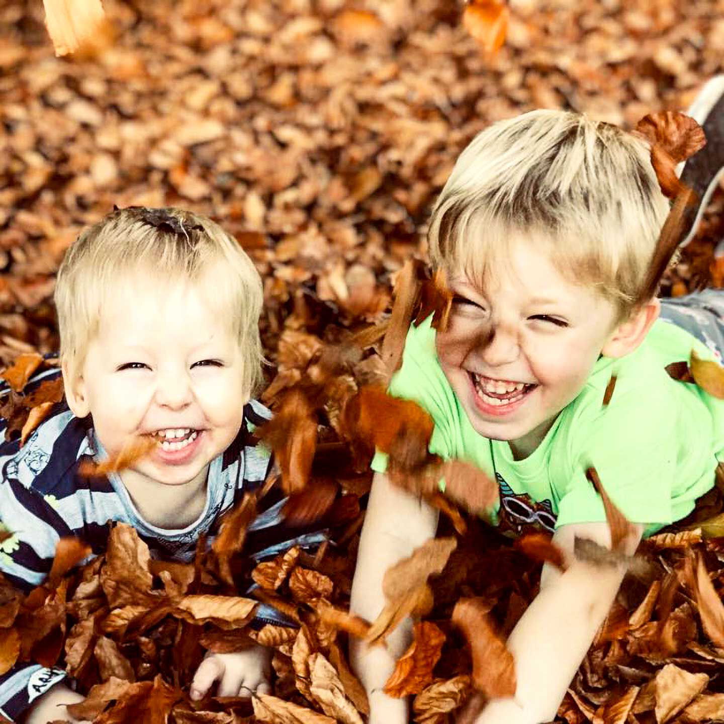 Zwei Kinder liegen lachend auf dem Waldboden im Laub.