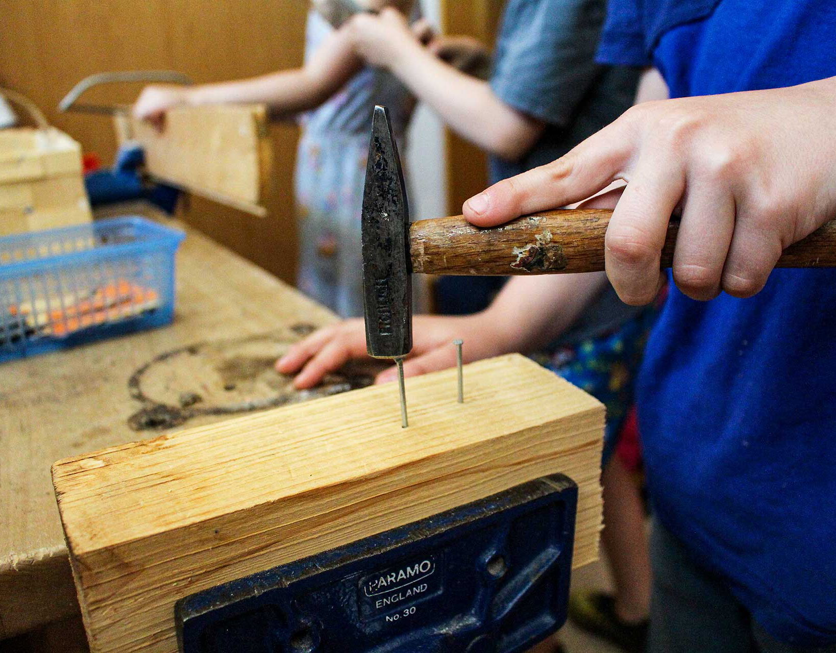 Ein Kleinkind schlägt einen Nagel in ein Holzstück in der Kinderwerkstatt.