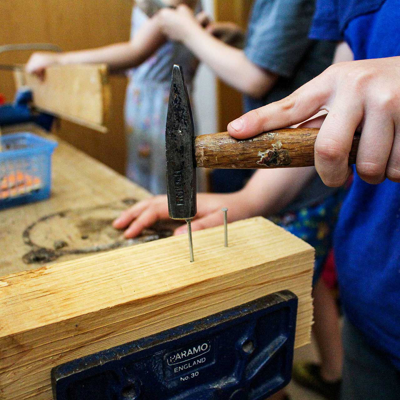 Ein Kleinkind schlägt einen Nagel in ein Holzstück in der Kinderwerkstatt.