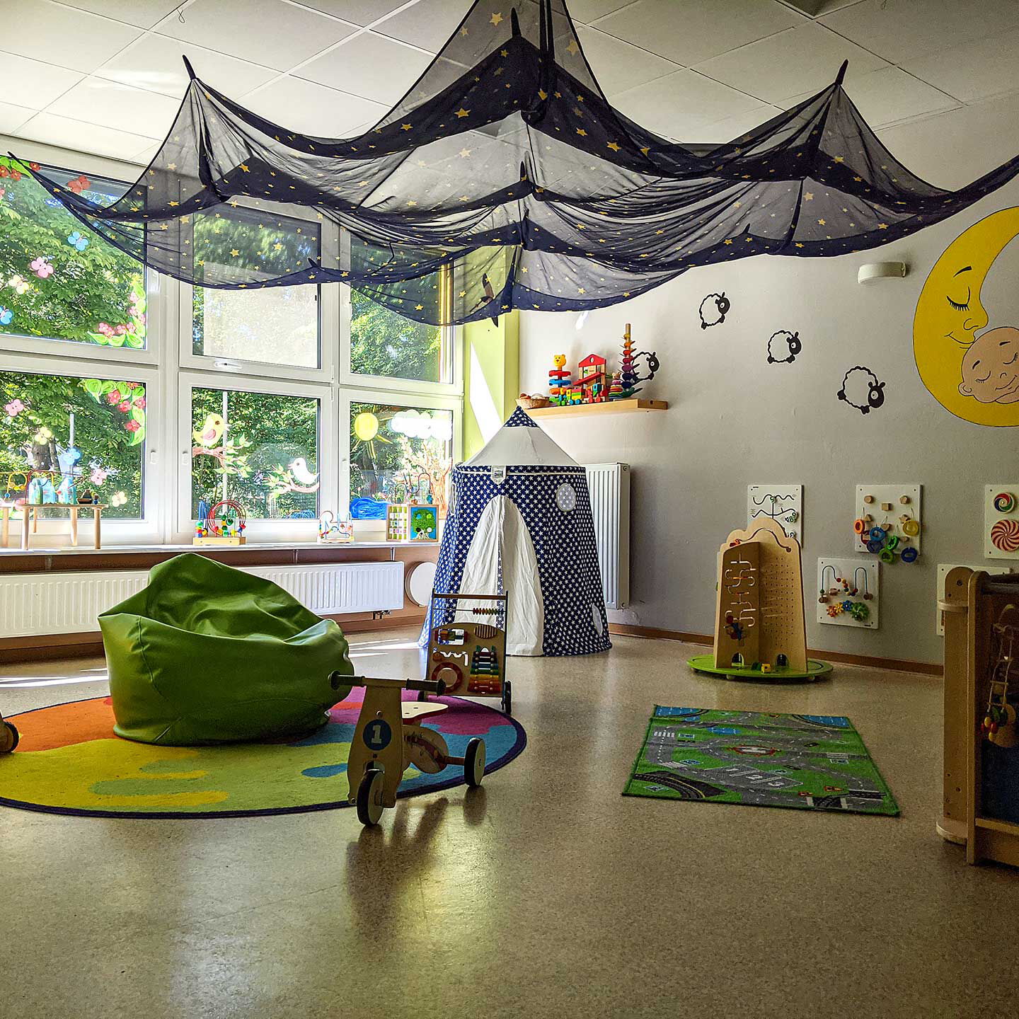 Das Gruppenzimmer im Kleinstkindbereich mit zwei Spielteppichen, Wandbildern, Holzspielzeug und einem Zelt.