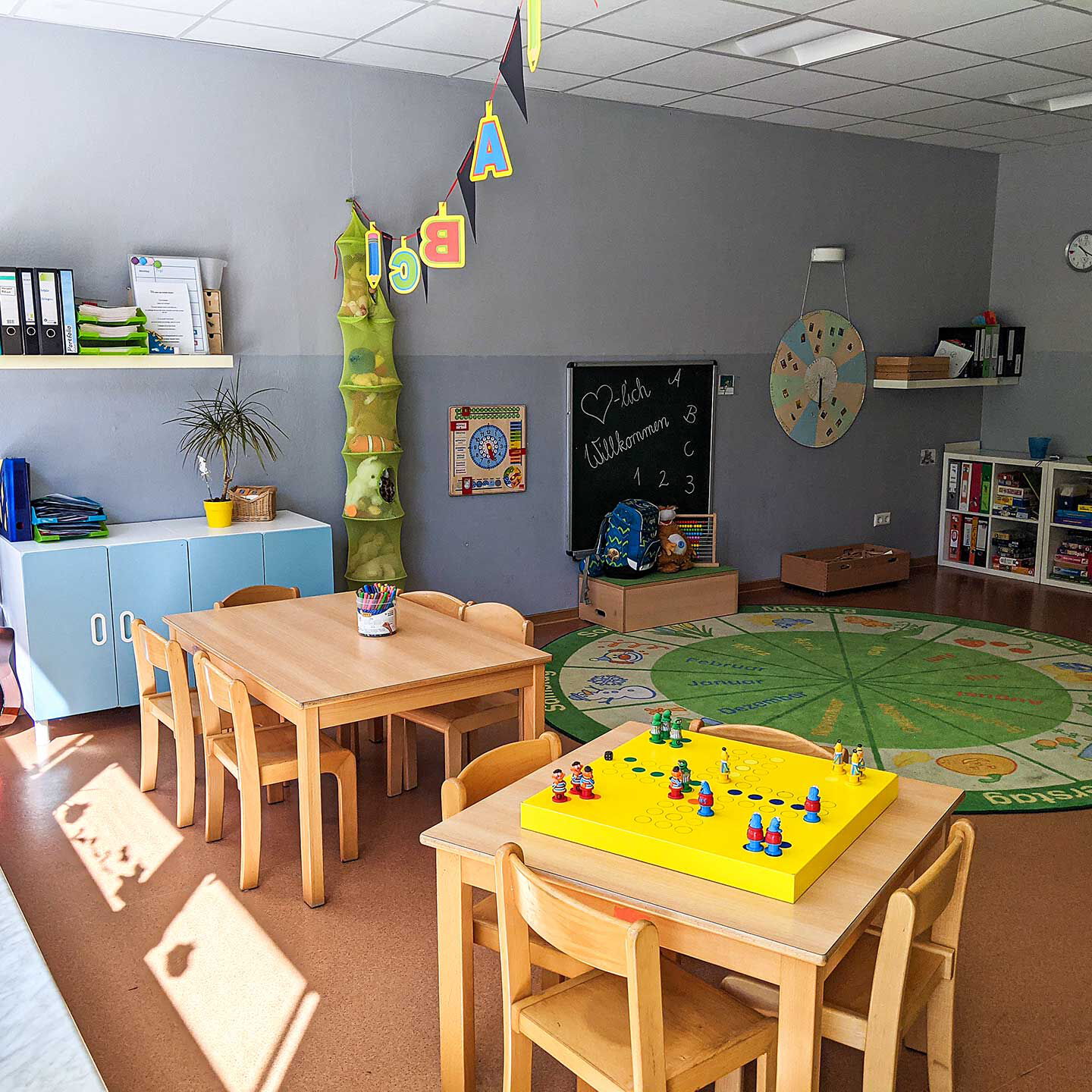 Das Gruppenzimmer der Vorschulgruppe mit zwei Tischen mit Stühlen, einer Wandtafel und Regalen mit Spielzeug.