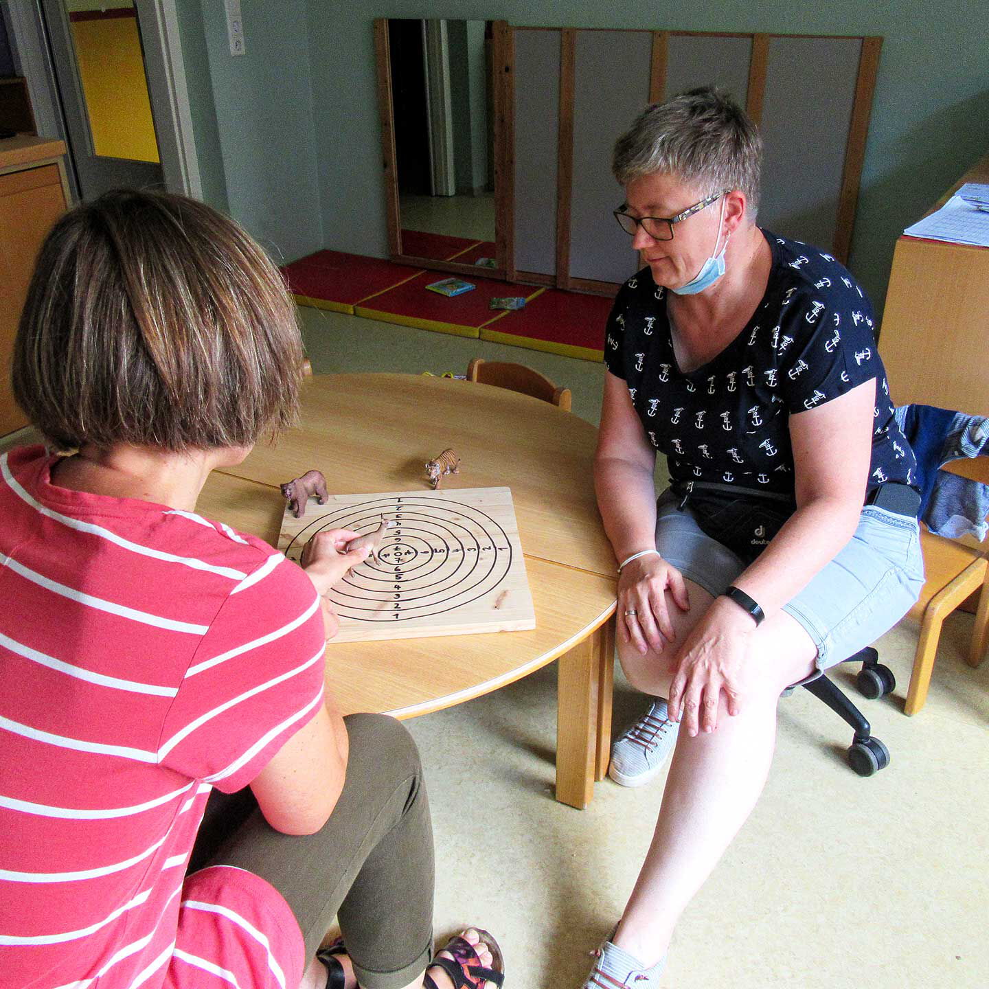 Zwei Frauen sitzen an einem Tisch im Büro und stellen mit Spielzeugtieren eine Aufstellung dar.