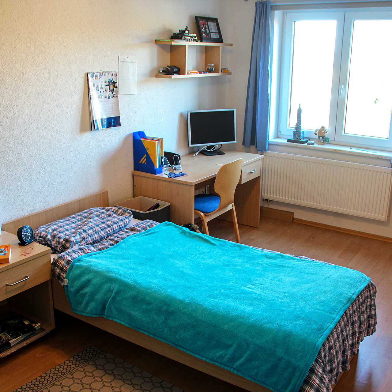Ein Einzelzimmer im Internat mit einem Bett, Schreibtisch und Kleiderschrank.