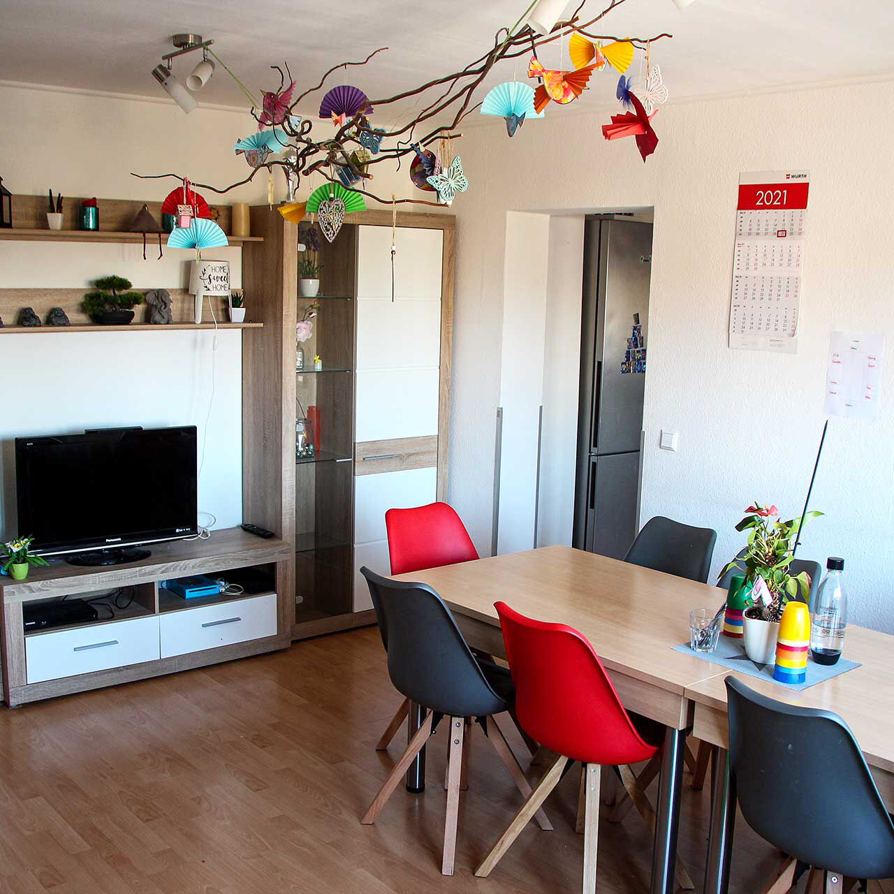 Das Gruppenzimmer mit zwei Tischen mit Stühlen, einer Anbauwand und TV.