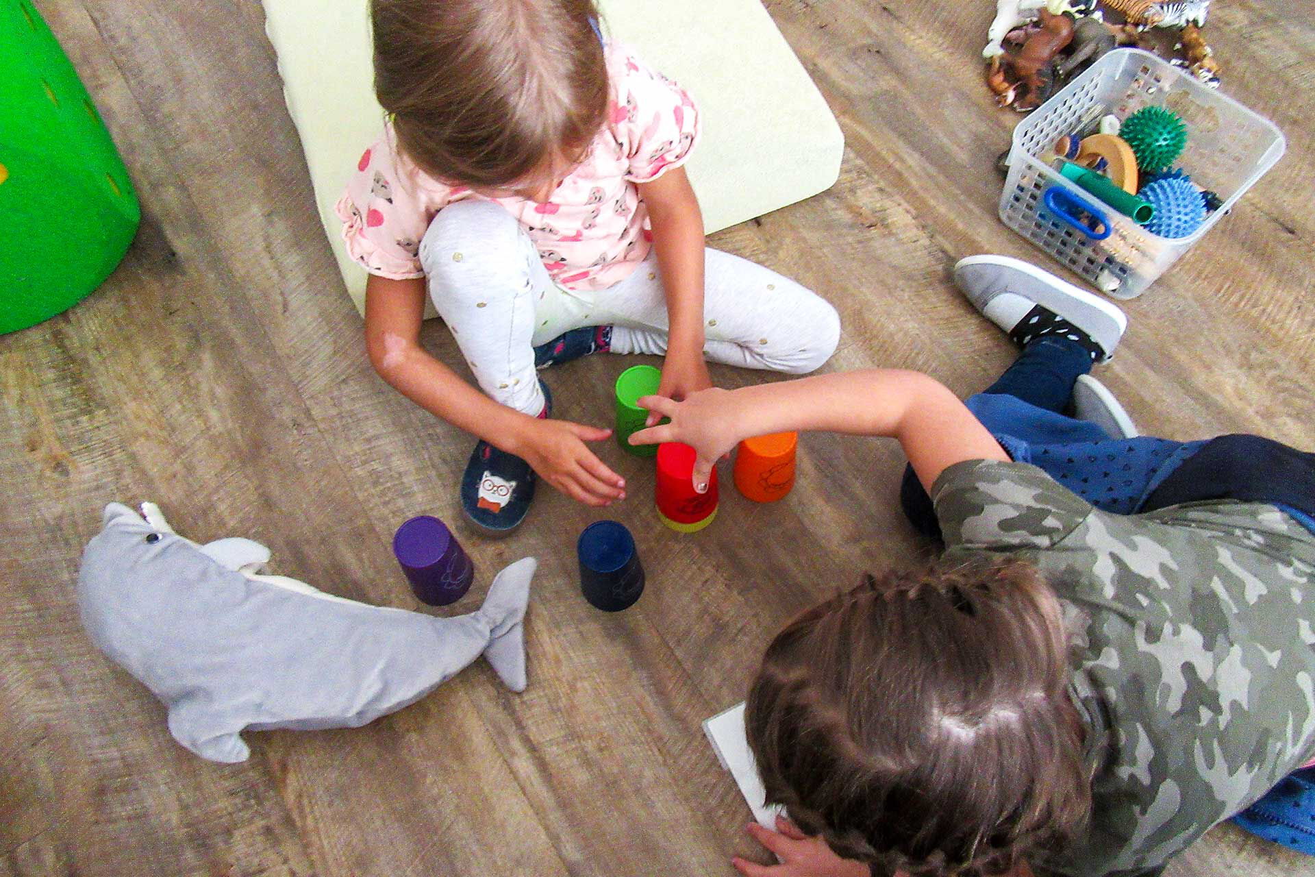 Zwei Kinder sitzen auf dem Fußboden und spielen mit den Stapelbechern.