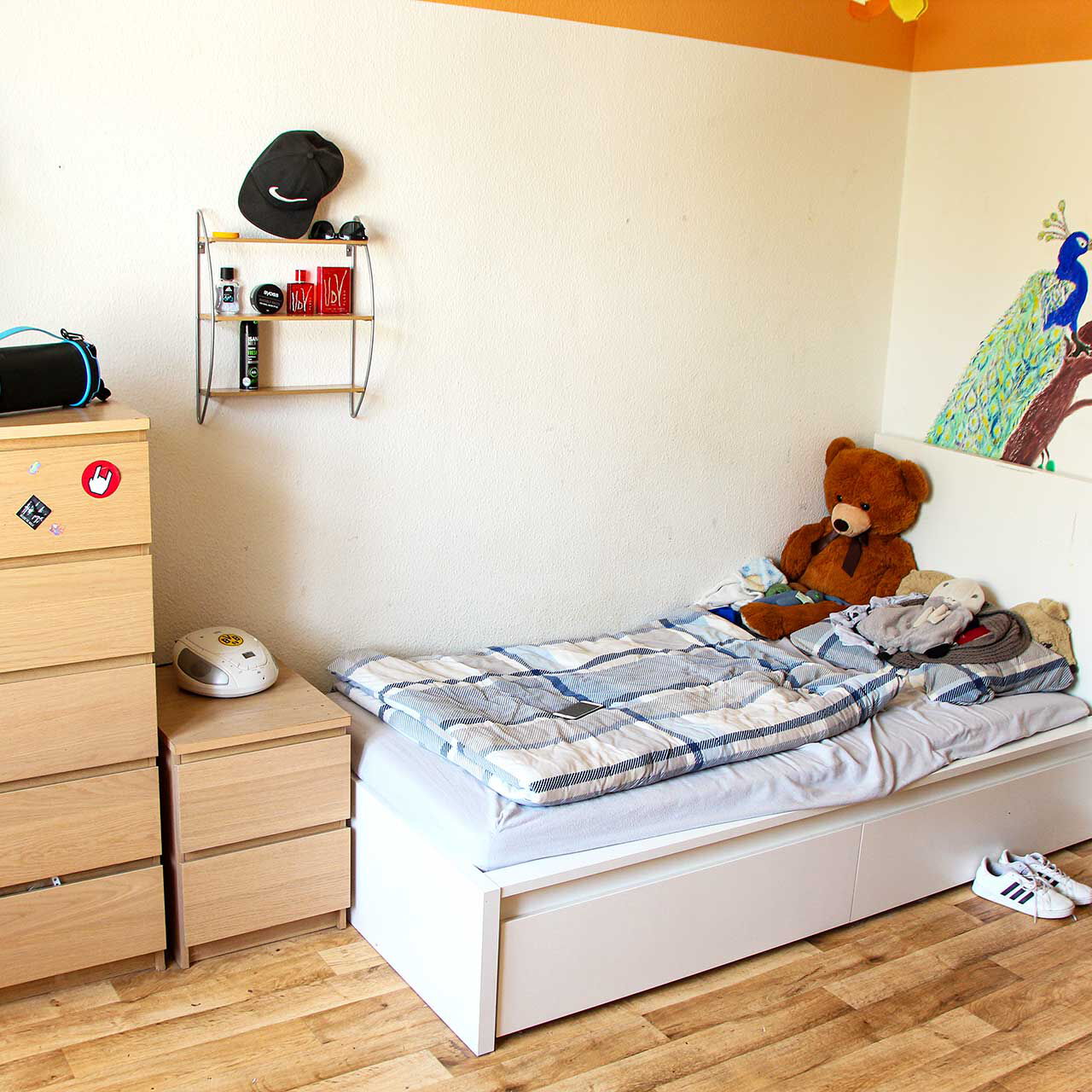 Ein Jugendzimmer mit einem Bett, einer Kommode und einem Nachttischschrank.